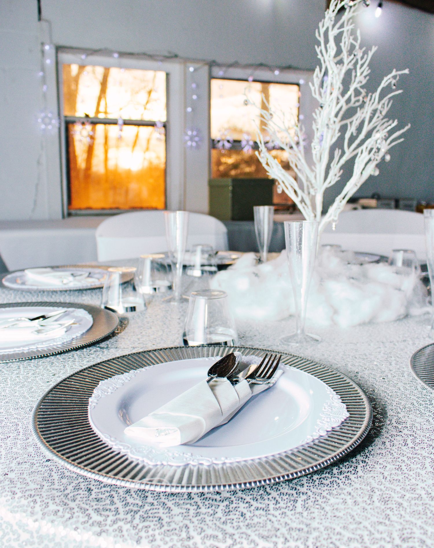 Elegant white winter table setting features a striped charger plate with silver branches in a modern minimalist style.