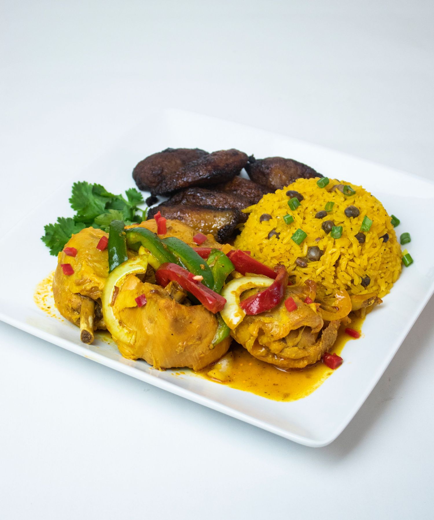 Yellow curry chicken with roasted portobello mushrooms and fresh herbs on white plate.