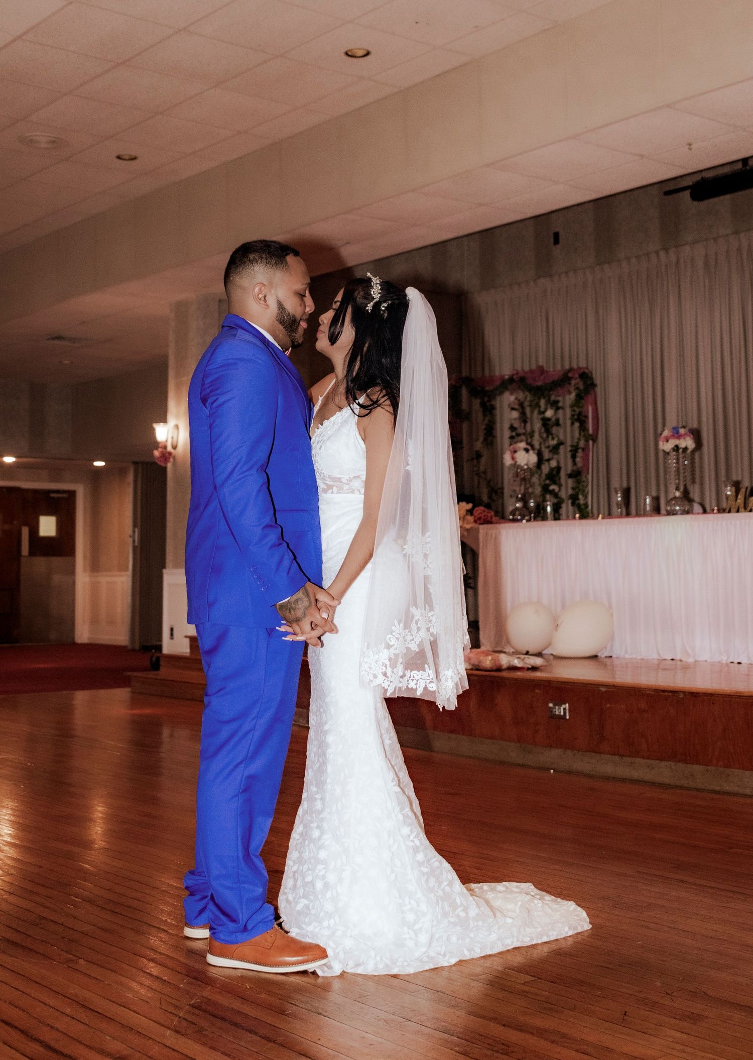 Couple shares an intimate moment during their wedding ceremony, with bride in white lace gown and groom in royal blue suit.