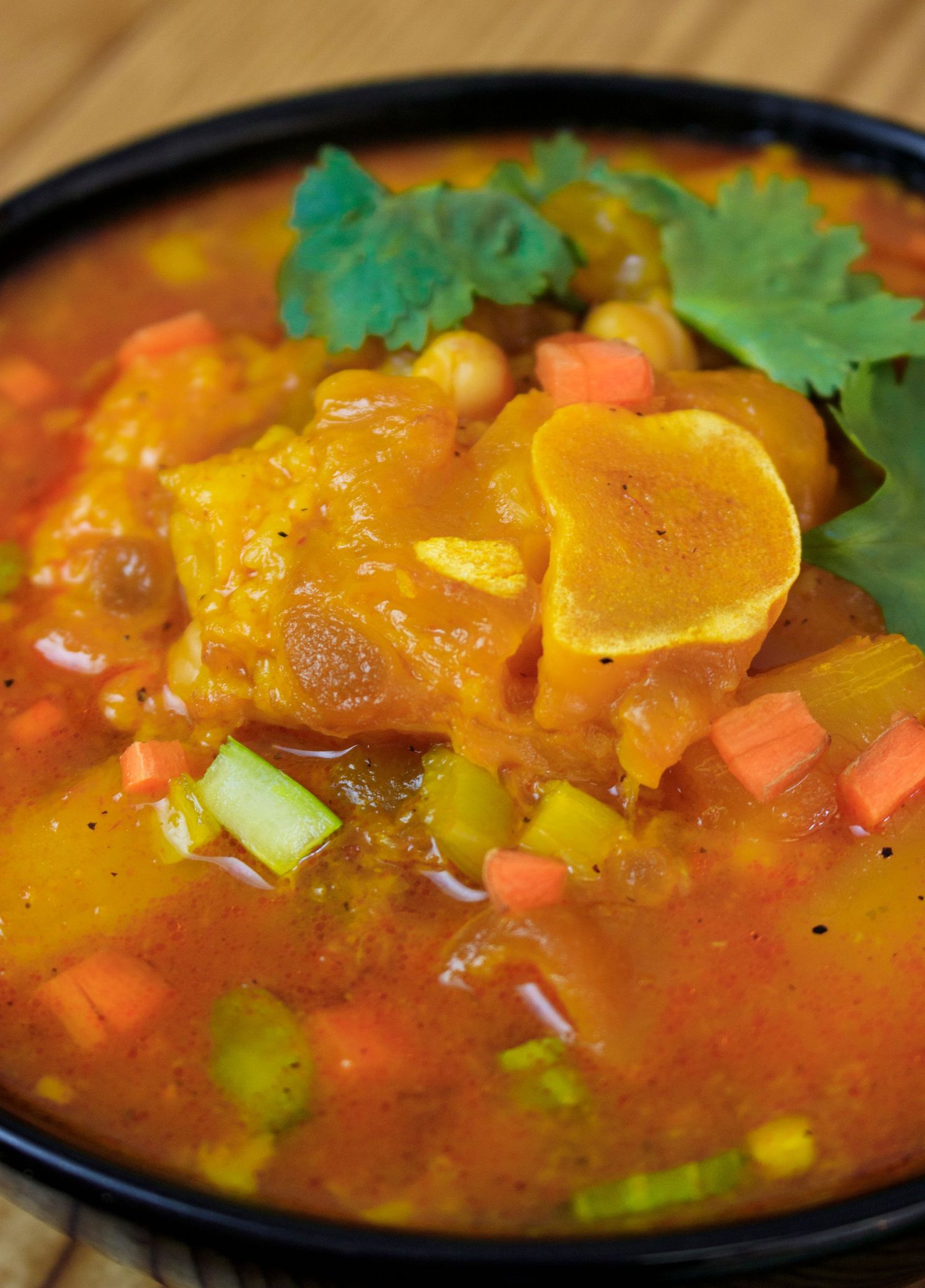 Spicy Caribbean curry soup with colorful vegetables and herbs in a black bowl.
