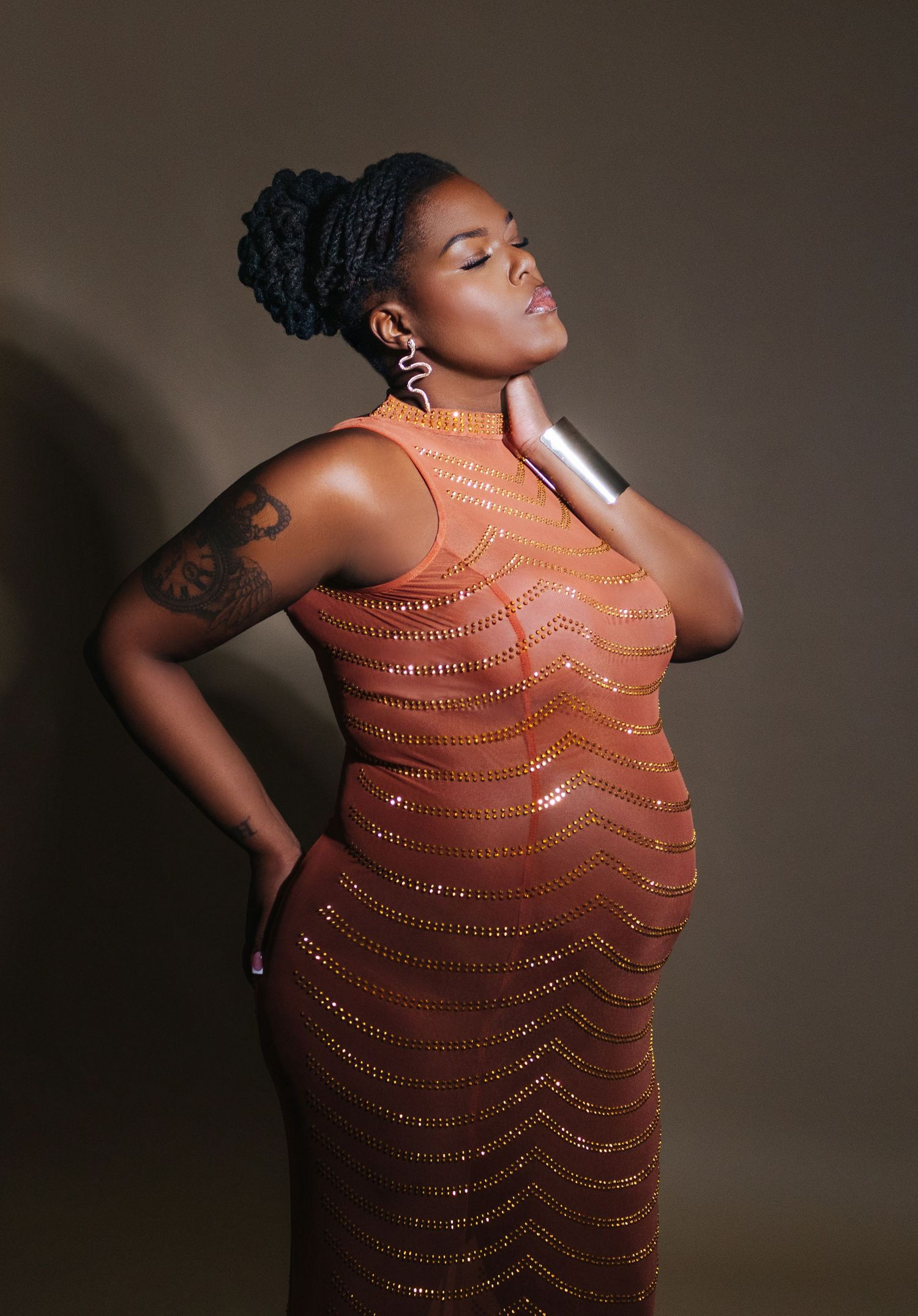 A dramatic portrait of a curvaceous figure in a shimmering copper dress against dark backdrop.