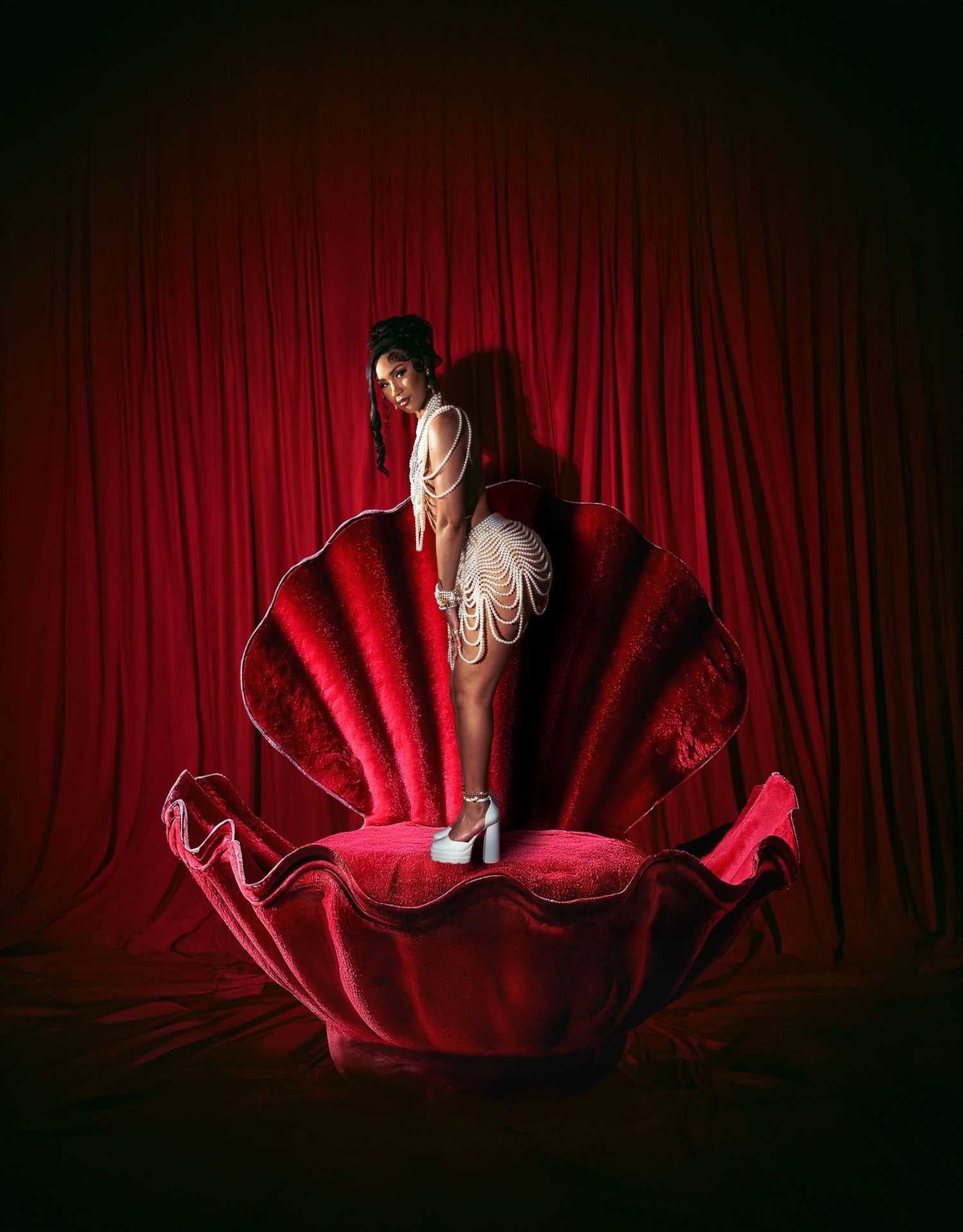 Theatrical portrait on large red velvet shell prop against dramatic curtain backdrop.