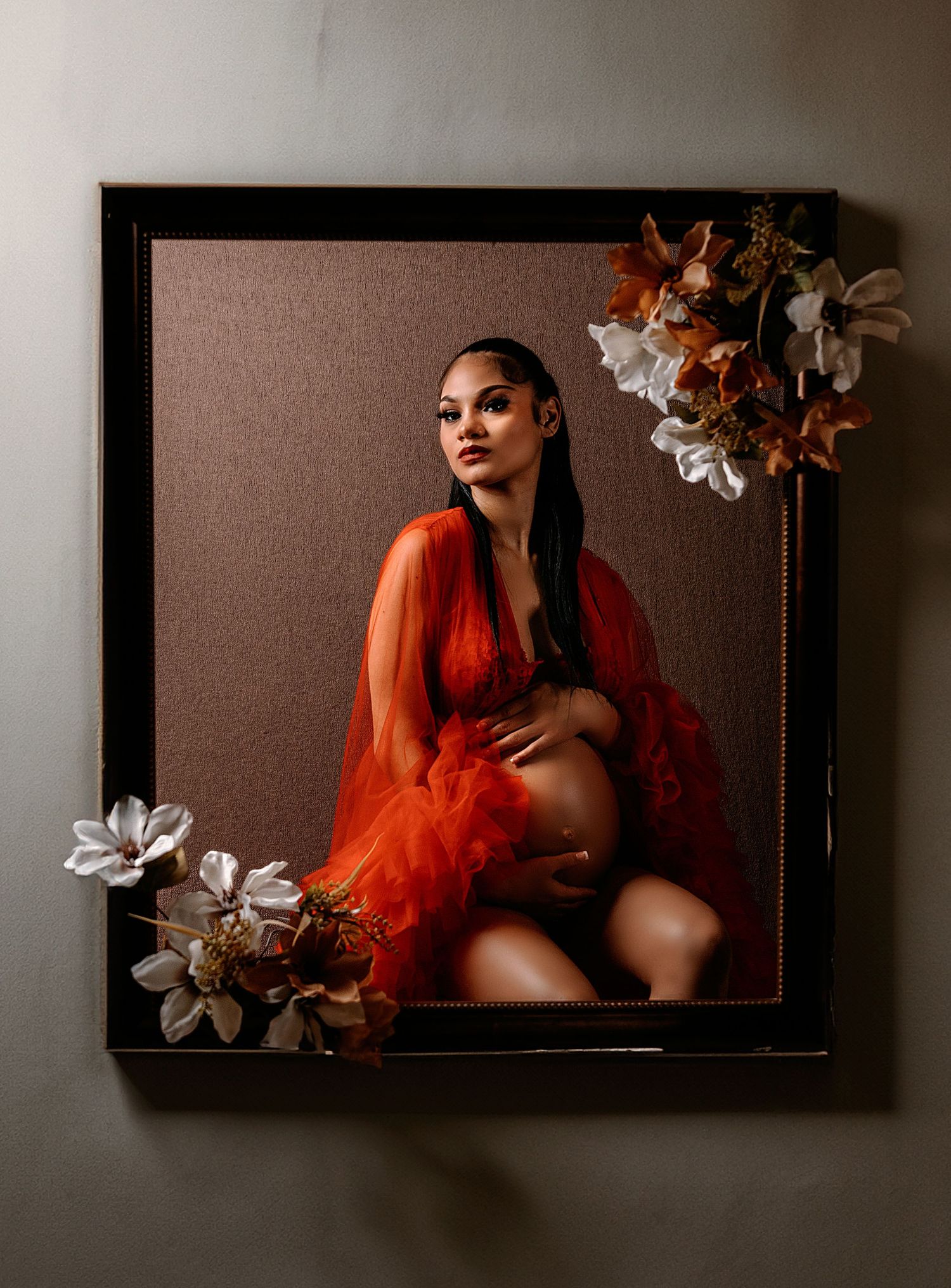 Framed maternity portrait with floral elements and red sheer dress.