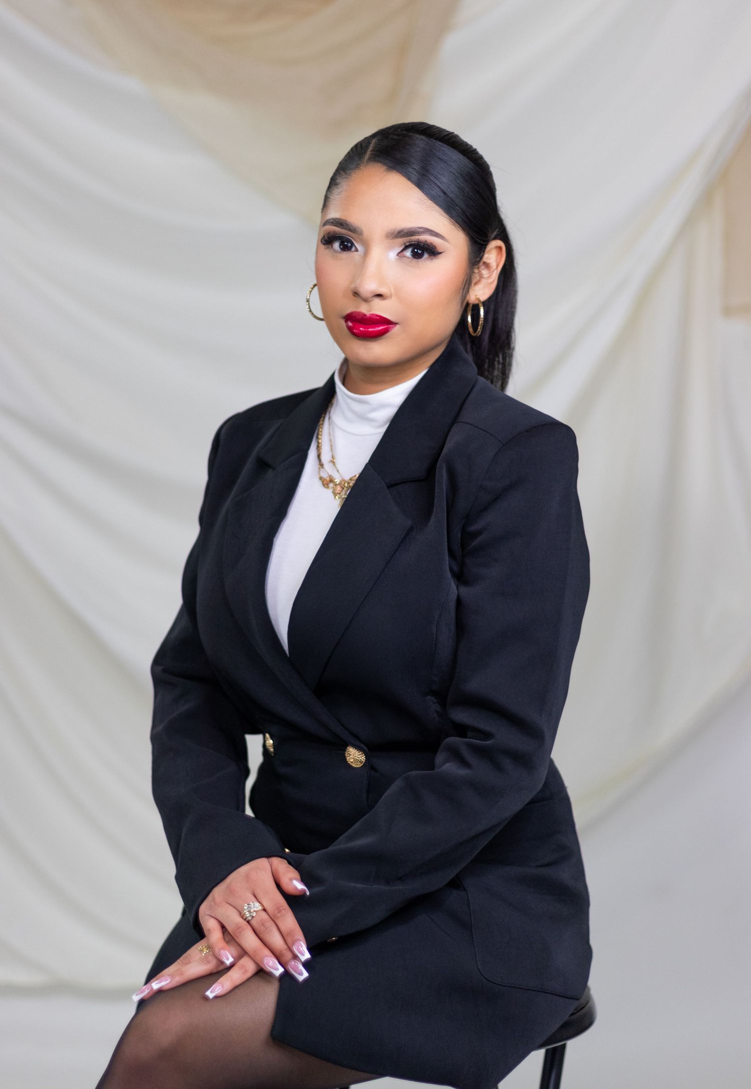 Professional portrait in black blazer with white top against draped fabric backdrop.