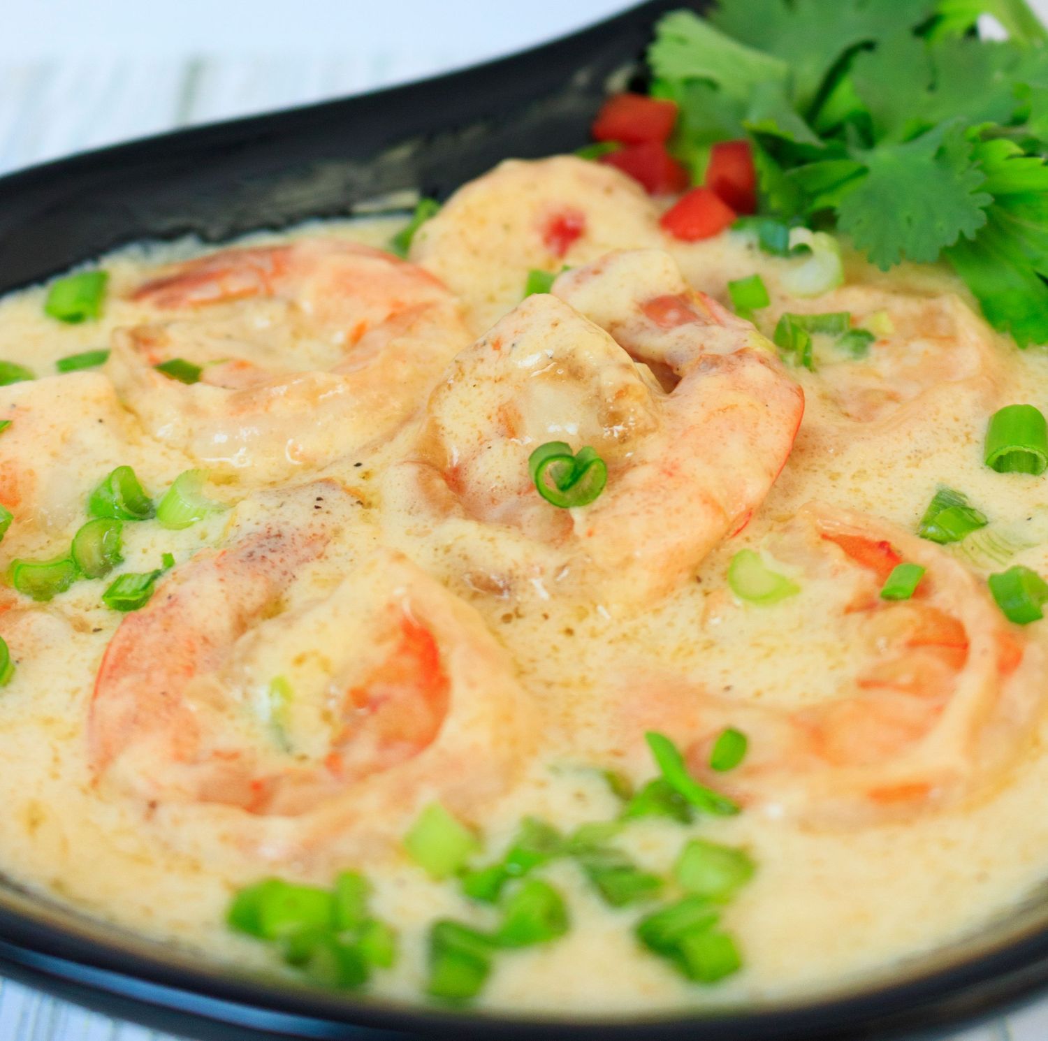 Shrimp in creamy sauce garnished with green onions and parsley in black dish.