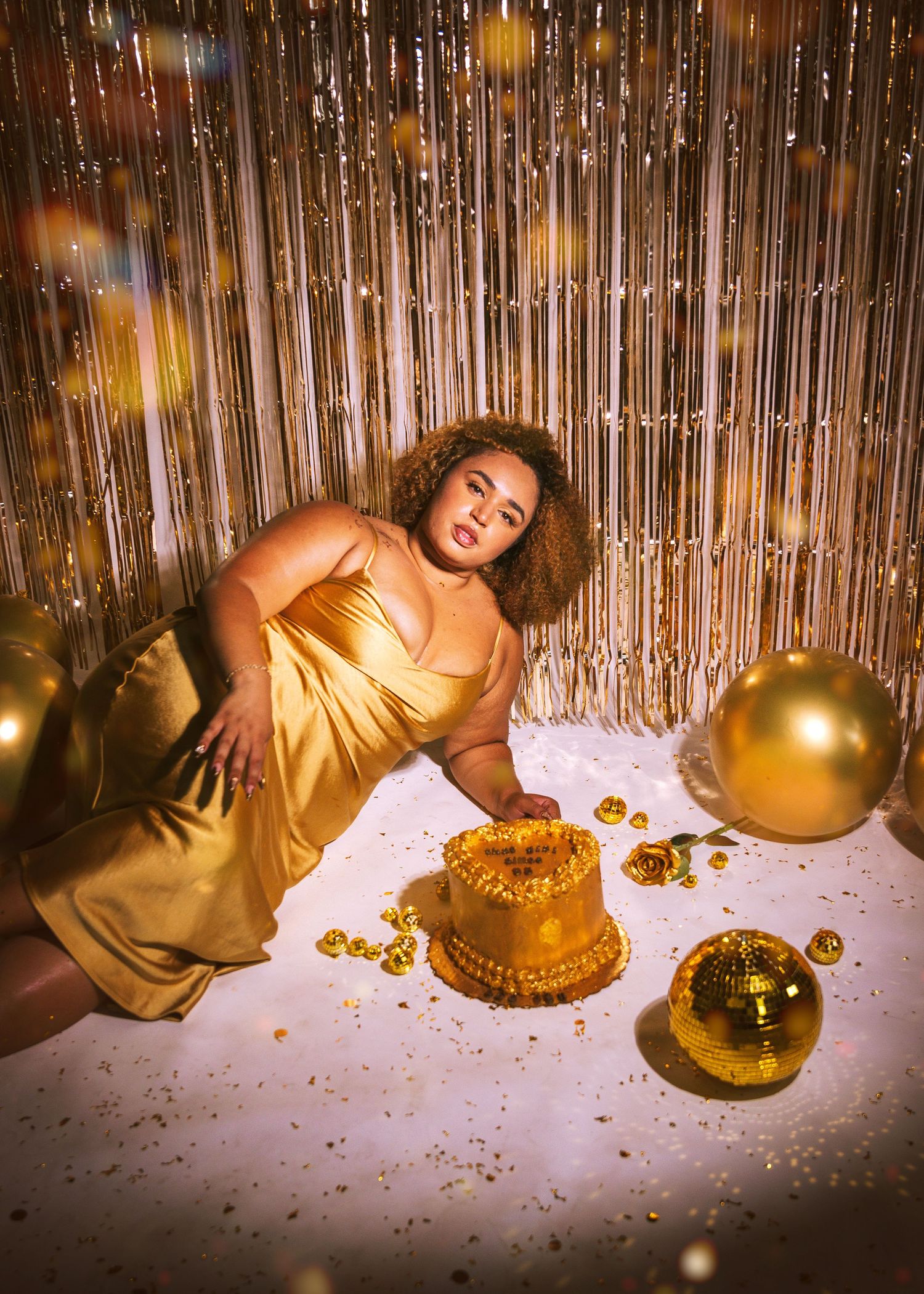 A glamorous celebration scene with gold balloons and decorations around a birthday cake.
