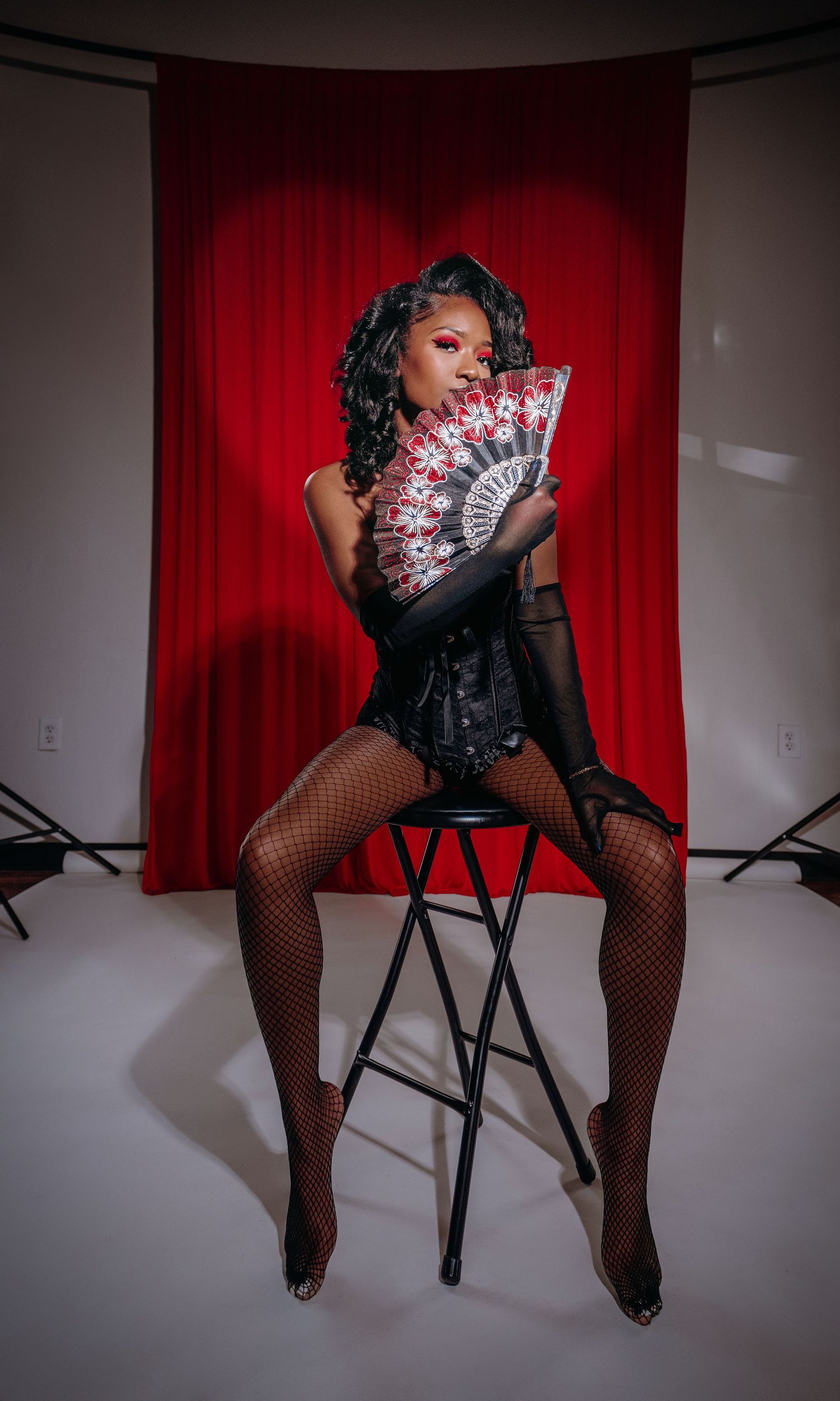 Dramatic portrait with decorative fan against red curtain backdrop.
