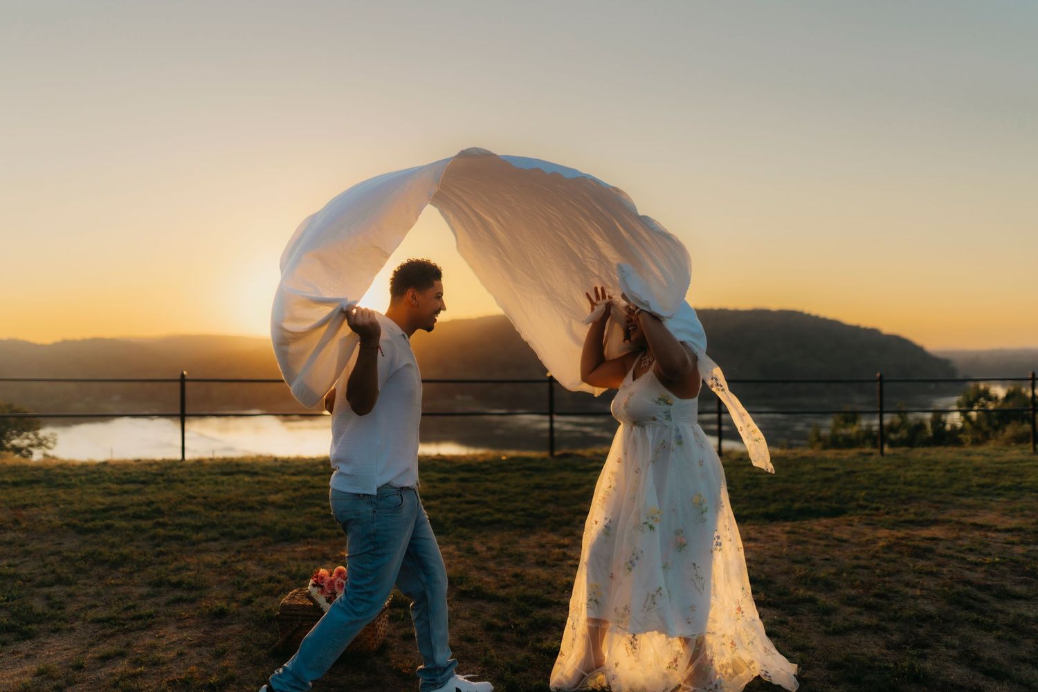 Couple in wedding attire dances together during golden sunset in an outdoor field.