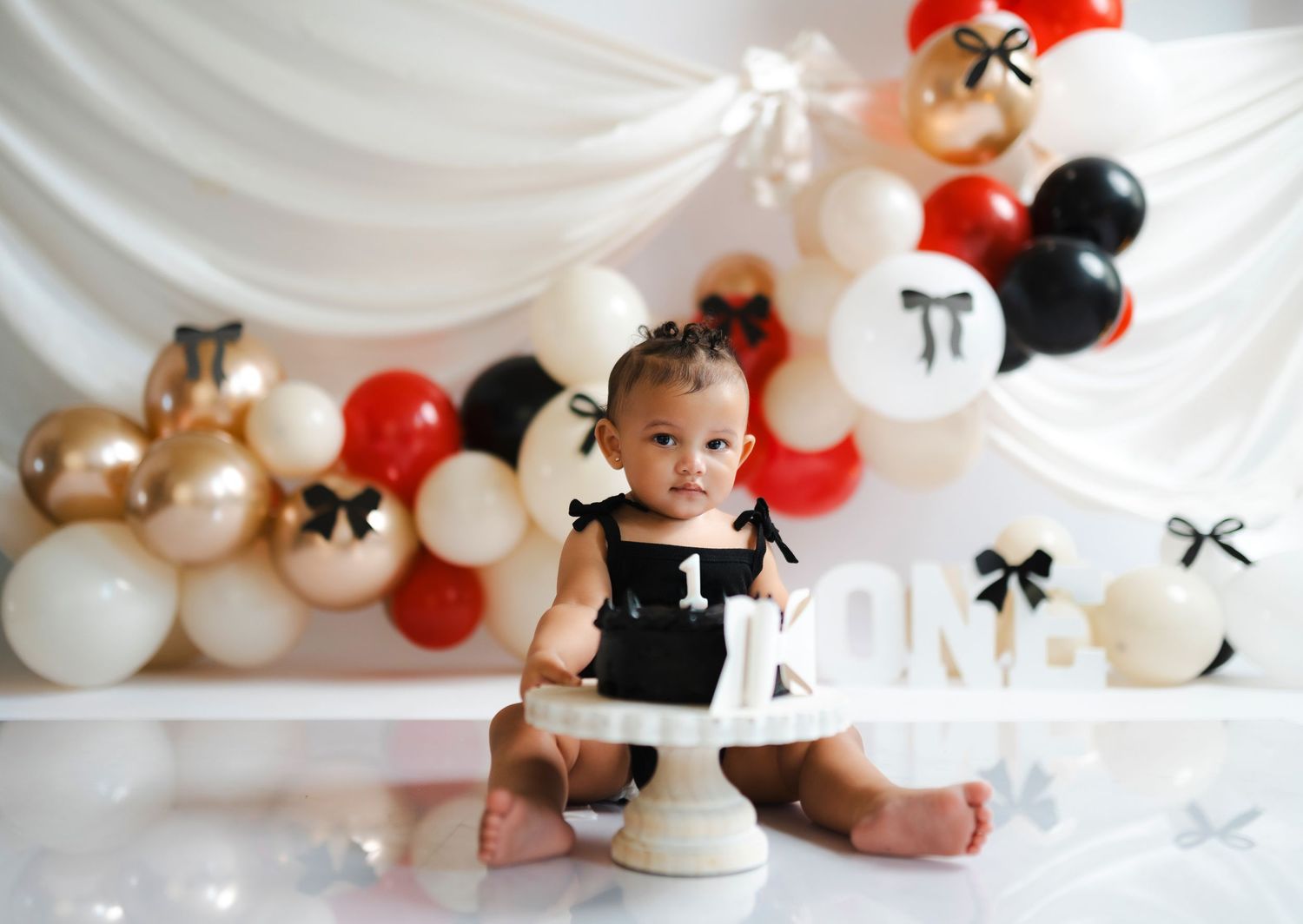 Elegant balloon arch installation in white, red, and black with bows and draped fabric backdrop for party decor.