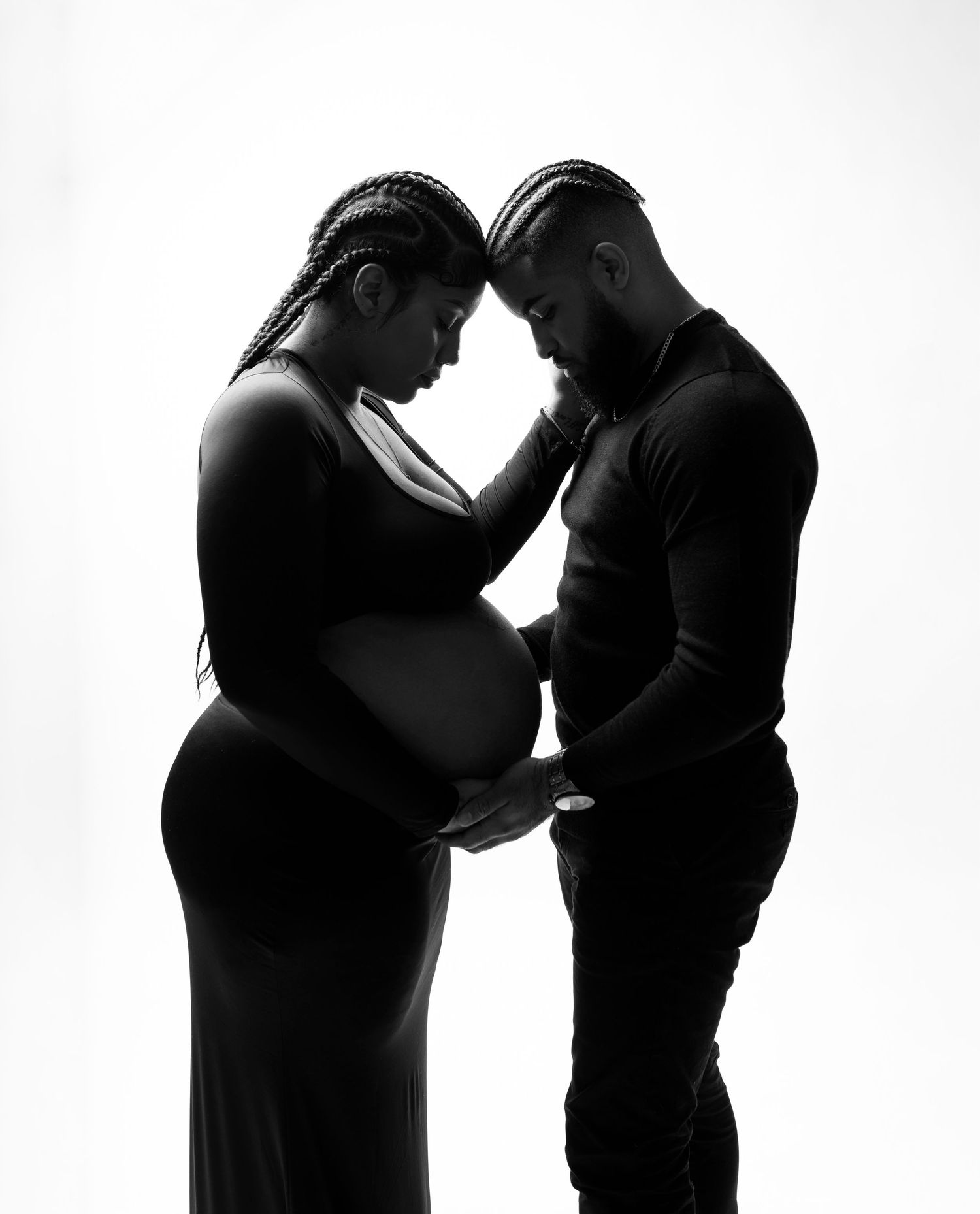 Dramatic silhouette of expectant couple sharing intimate moment against white background.