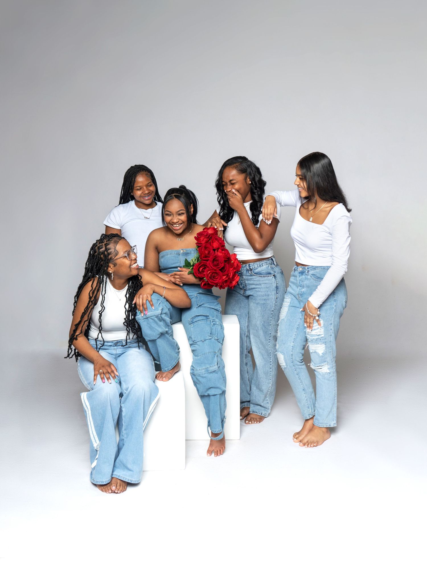 Four friends in matching denim jeans strike playful poses against a white studio backdrop in a progressive photo series.
