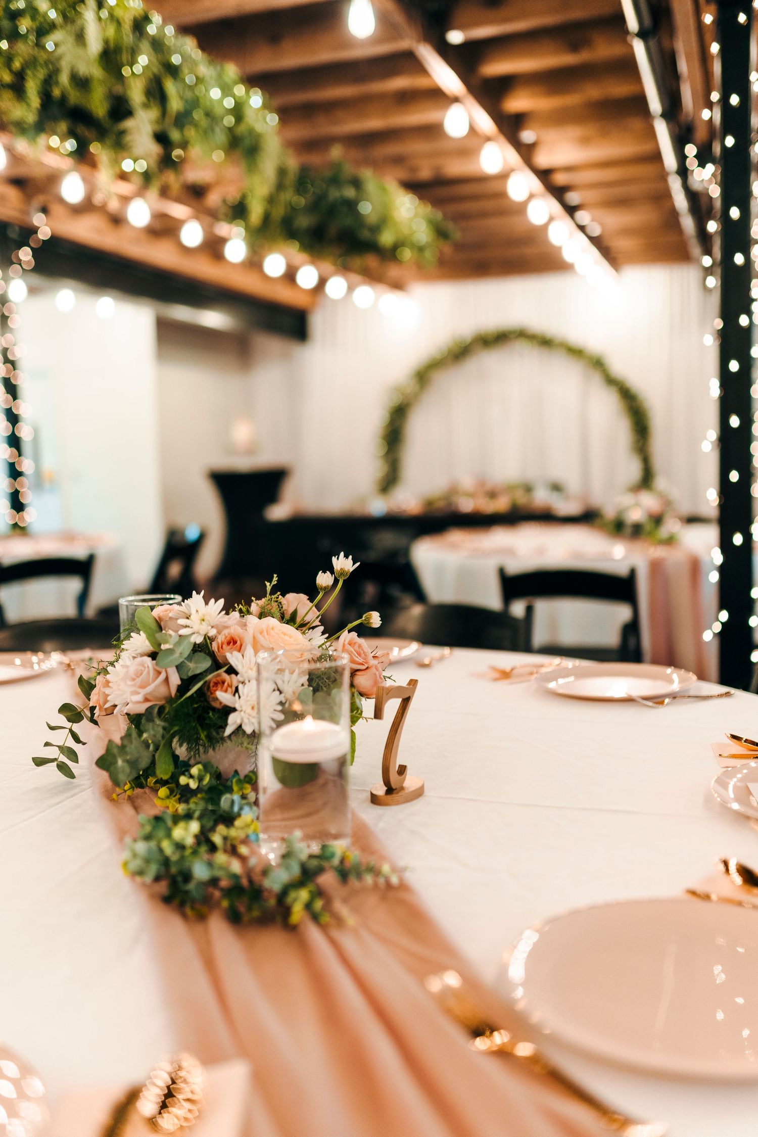 Elegant wedding reception table setup with string lights overhead and delicate floral centerpieces on white linens.