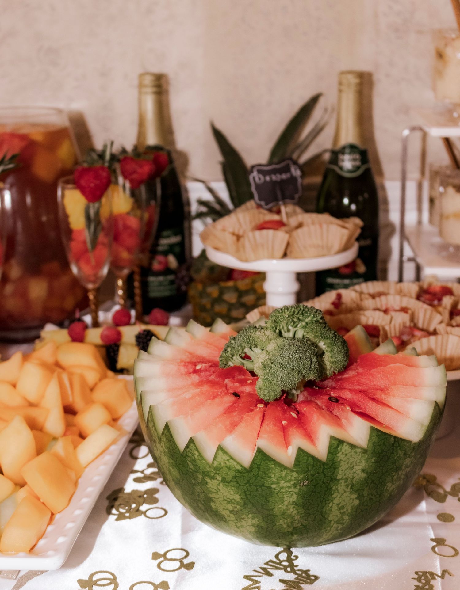 Watermelon carved into flower shape with fresh fruit and cocktails at wedding reception buffet.