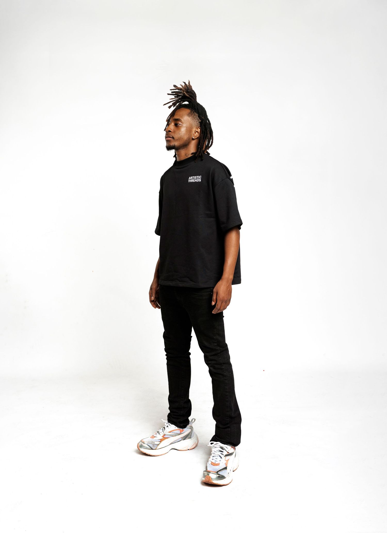 Casual streetwear look featuring black t-shirt, dark pants and multicolored sneakers against white backdrop.