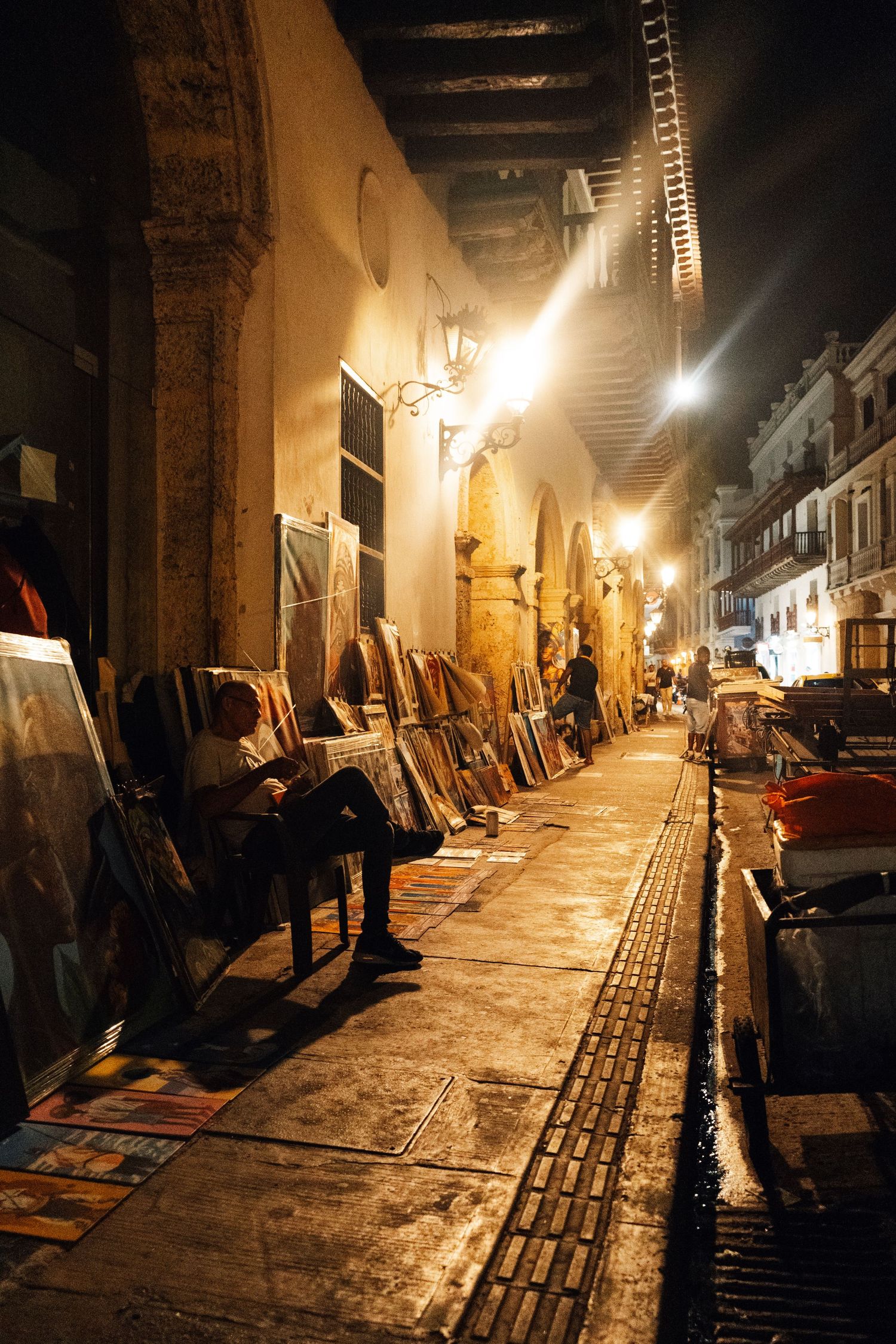 Atmospheric nighttime street scene with illuminated archways and vendor stalls along cobblestone path.