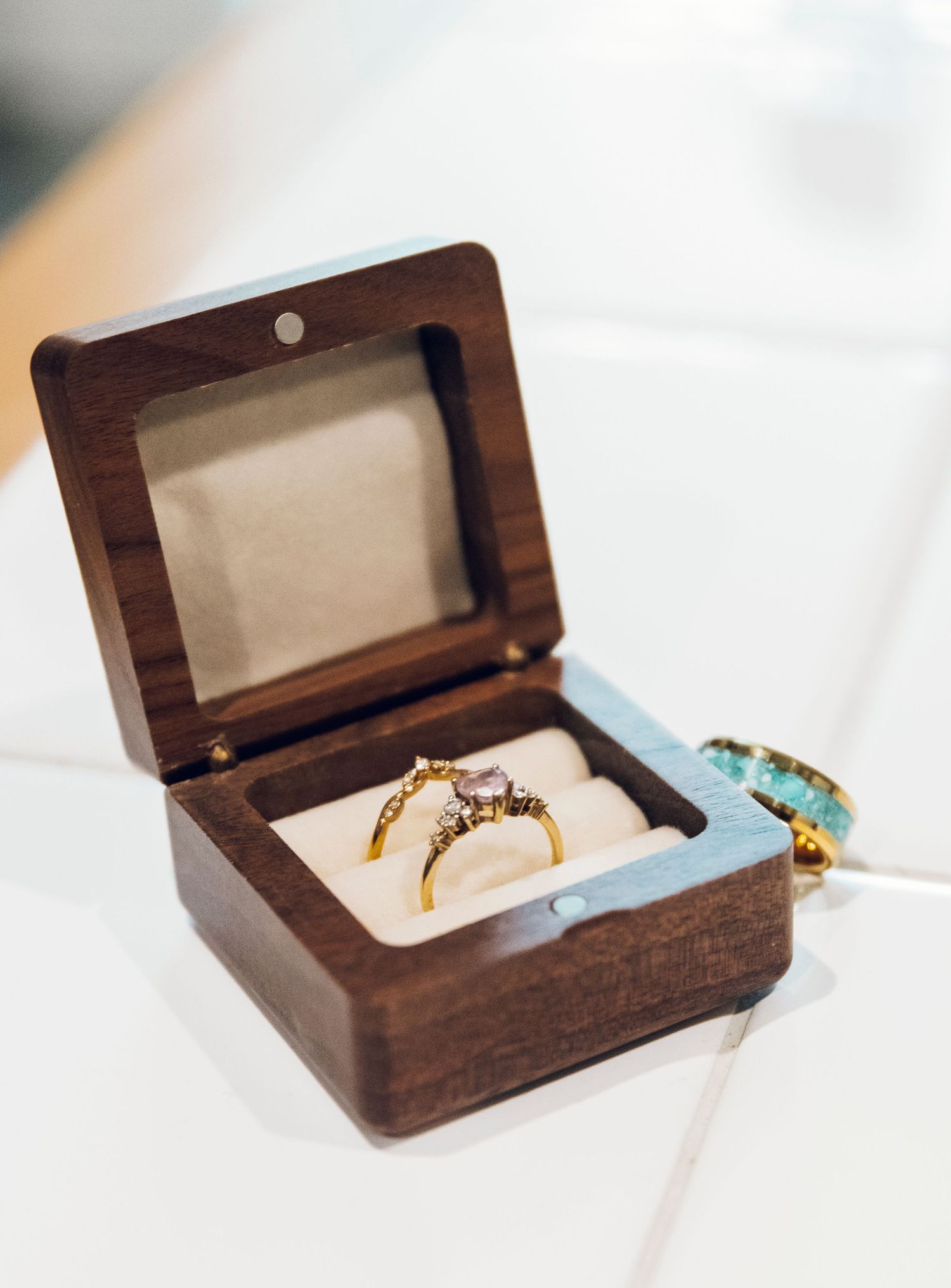 Two elegant engagement rings displayed in a small wooden ring box with velvet lining.