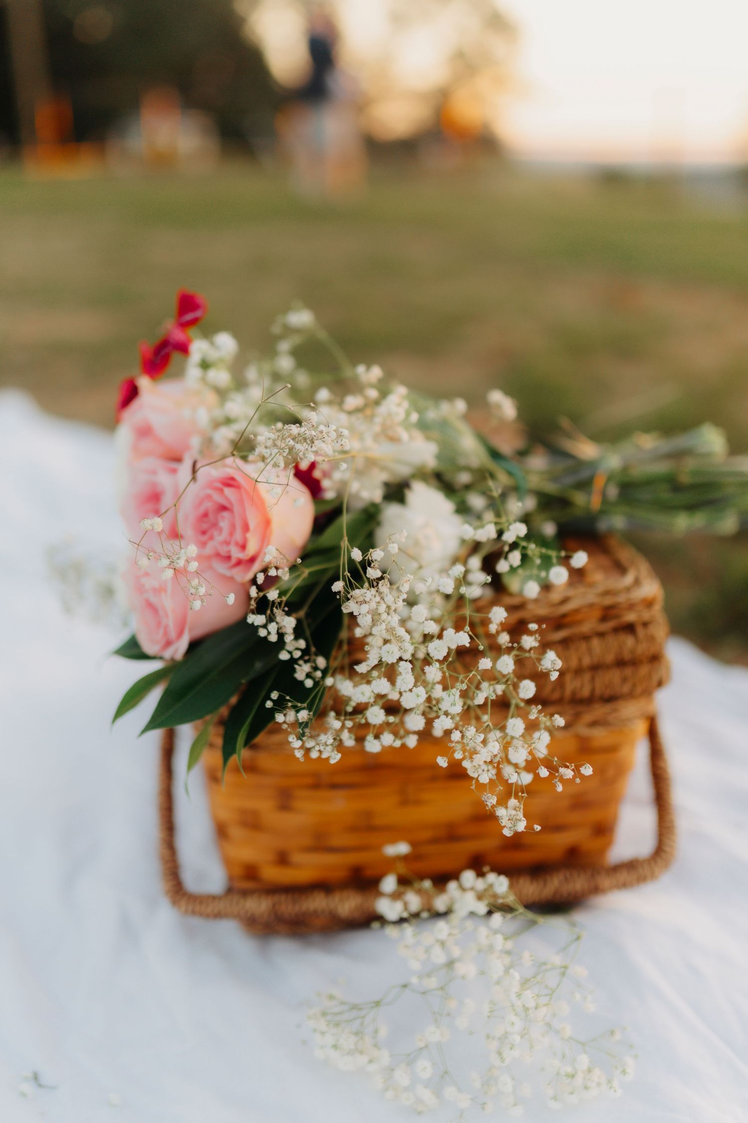 A rustic woven basket decorated with delicate pink roses and baby's breath flowers sits on a white surface.