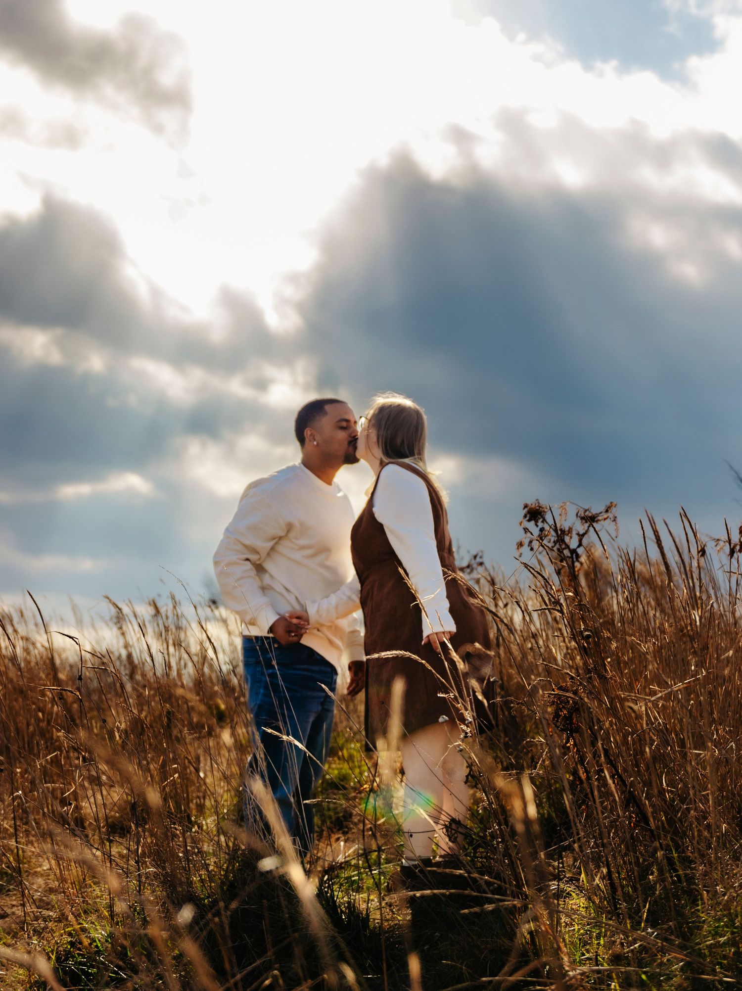 A couple shares a romantic moment standing among tall golden wheat fields under dramatic cloudy skies.