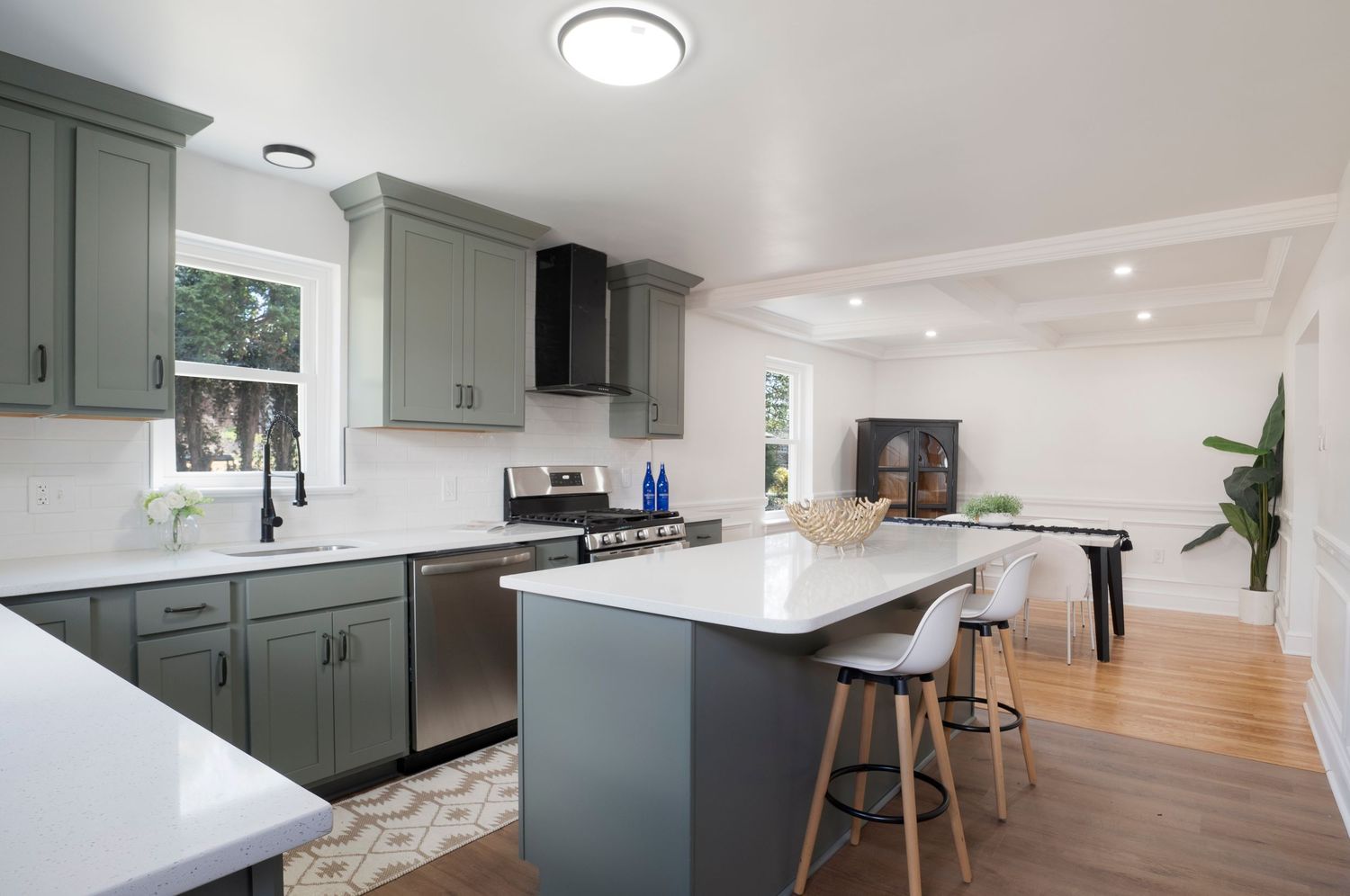 Modern kitchen with gray cabinets, white quartz countertops, stainless steel appliances, and an island with bar seating.