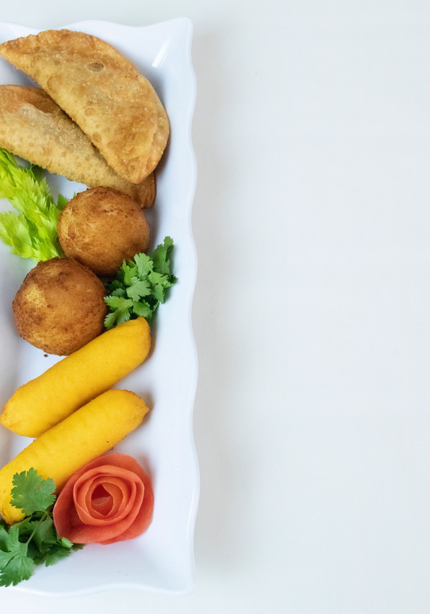 Empanadas and croquettes plated with mango slices and garnished with herbs on white rectangular dish.