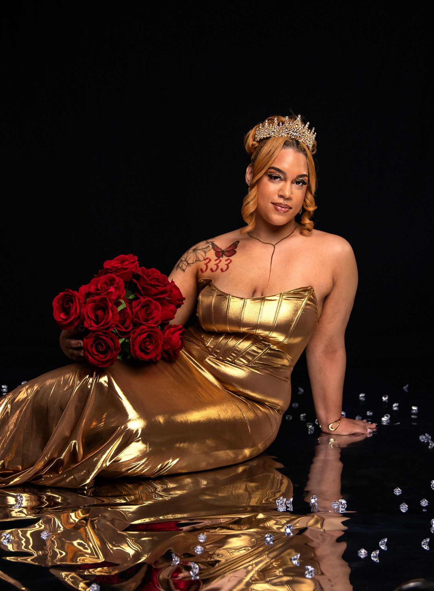 A regal portrait in a gold gown with red roses and a crown against a dark background.