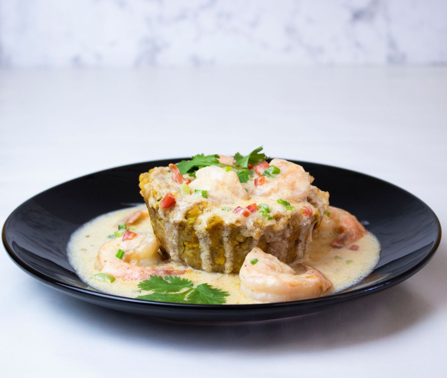 Stuffed artichoke with shrimp in cream sauce garnished with fresh herbs on black plate.