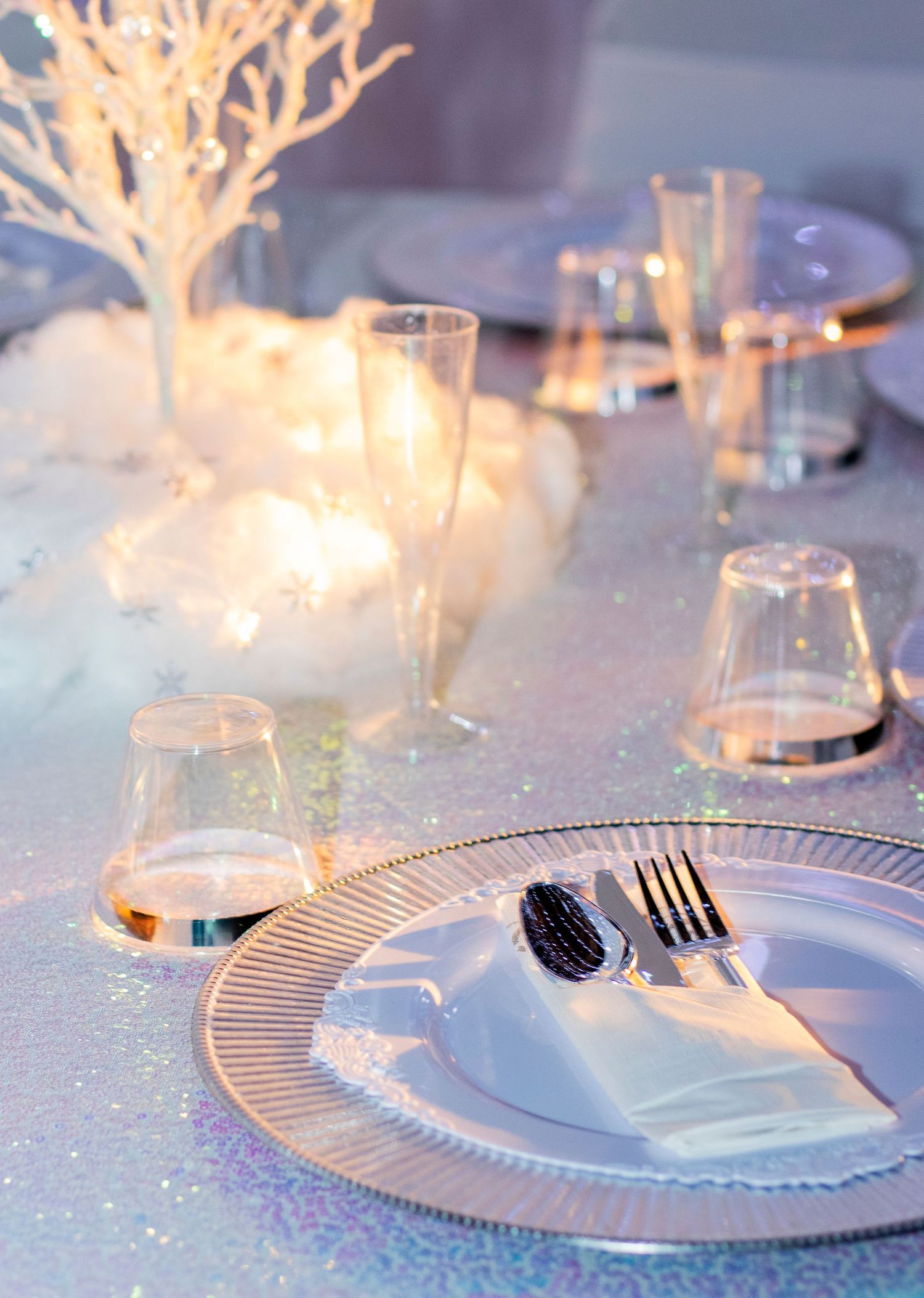 An elegant winter white table setting with glowing coral-like branches and sparkling glassware against a frosty backdrop.