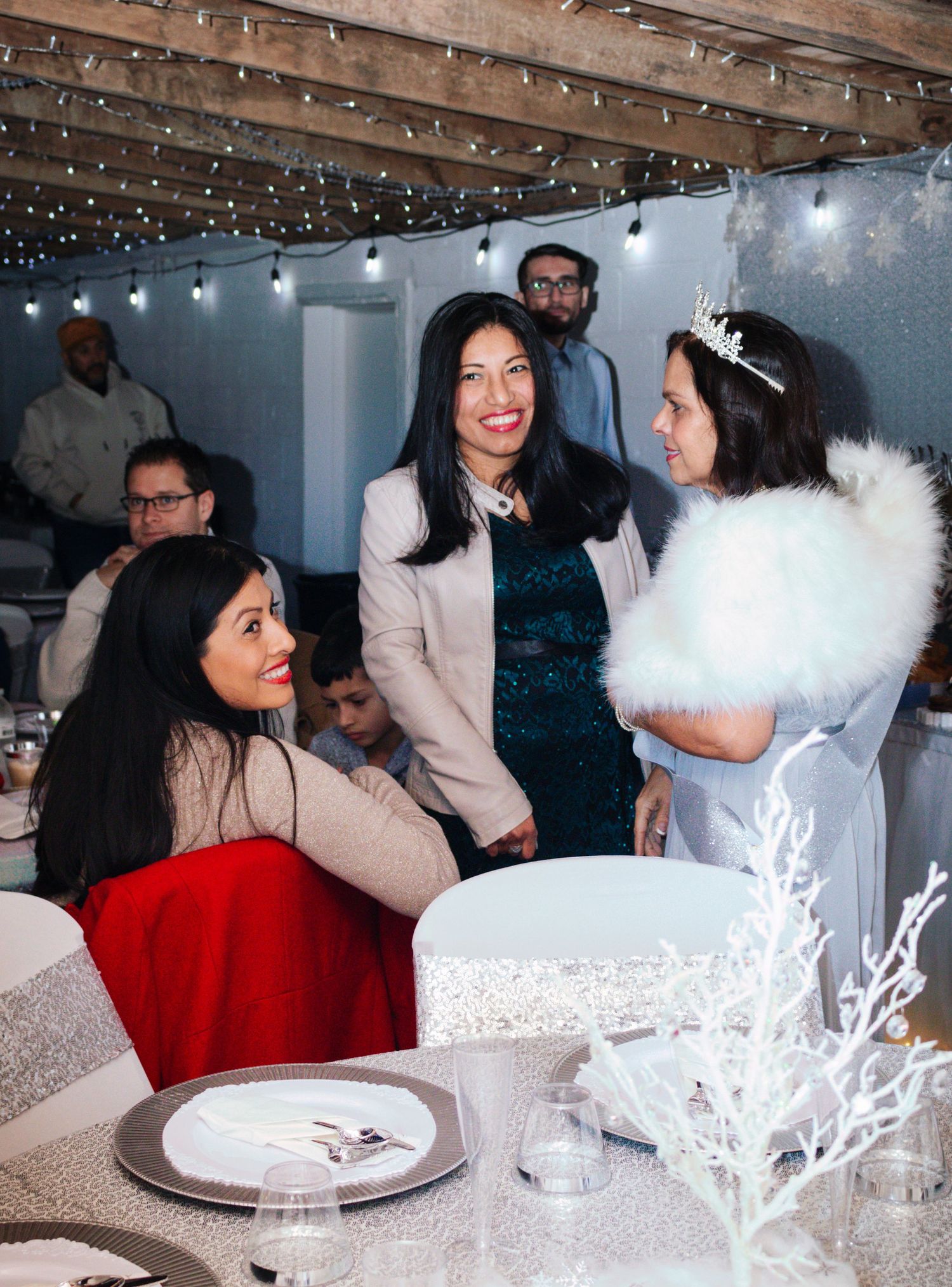 Guests mingle and celebrate at an elegant winter-themed party with white decor and twinkling lights overhead.