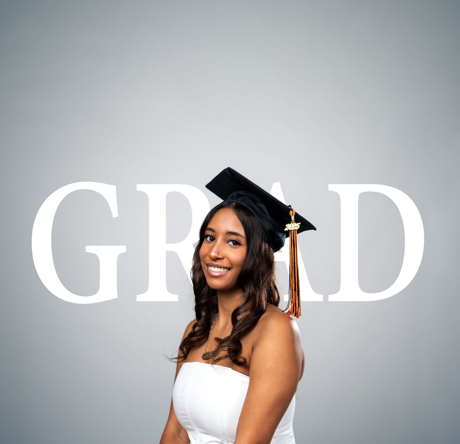 Graduate in cap and gown poses in front of large GRAD text on grey background.