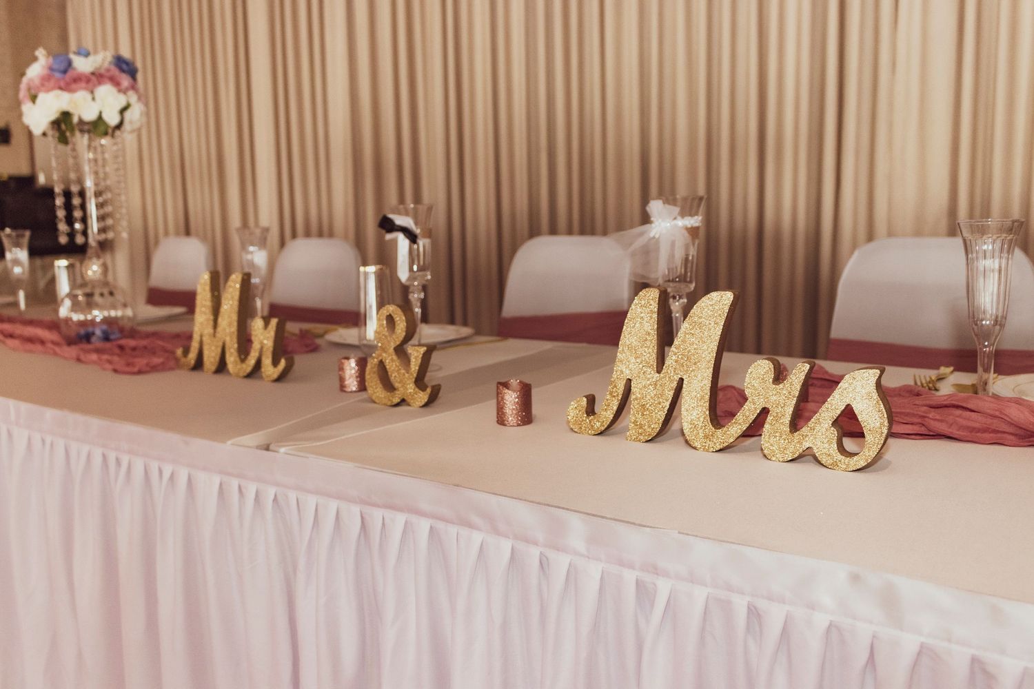 Gold 'Mr & Mrs' letters displayed on white tablecloth at wedding reception table.