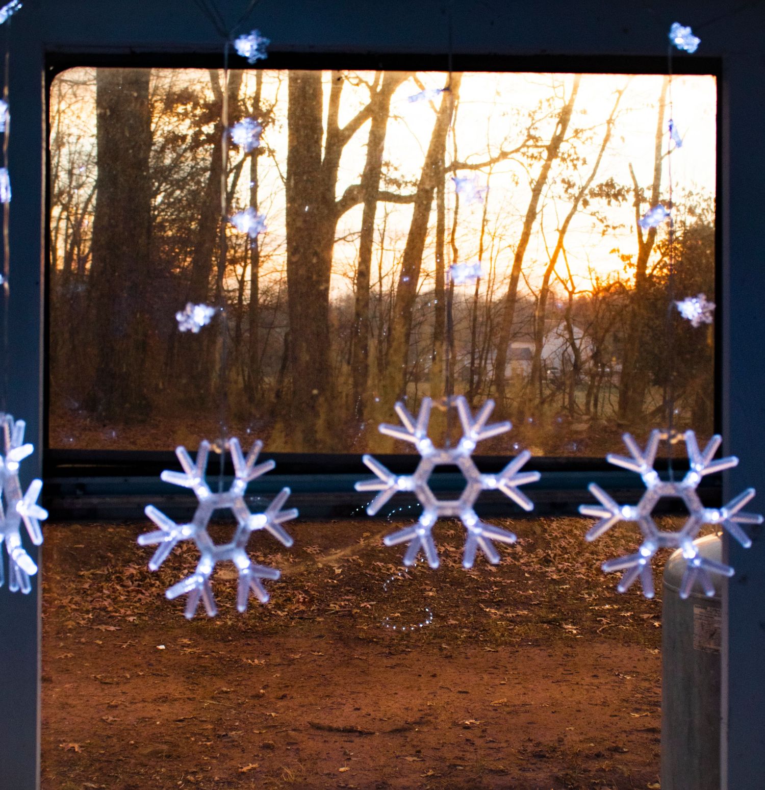 Illuminated snowflake decorations line a wooded path at dusk creating a magical winter lighting display.
