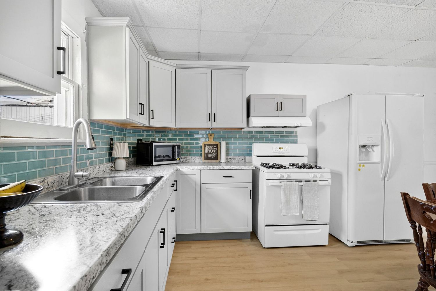 White kitchen with granite countertops, teal tile backsplash, white appliances, and light wood floors.
