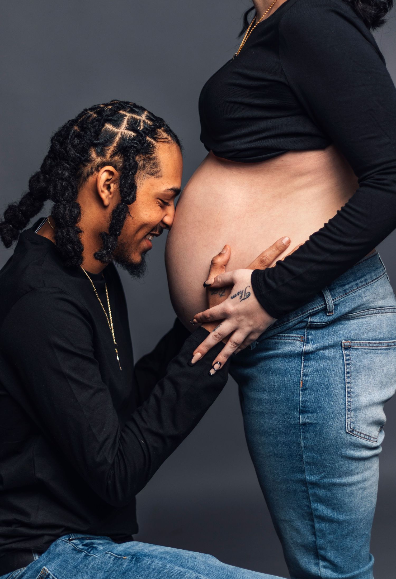 Intimate pregnancy photo with partner lovingly touching baby bump against dark grey background.