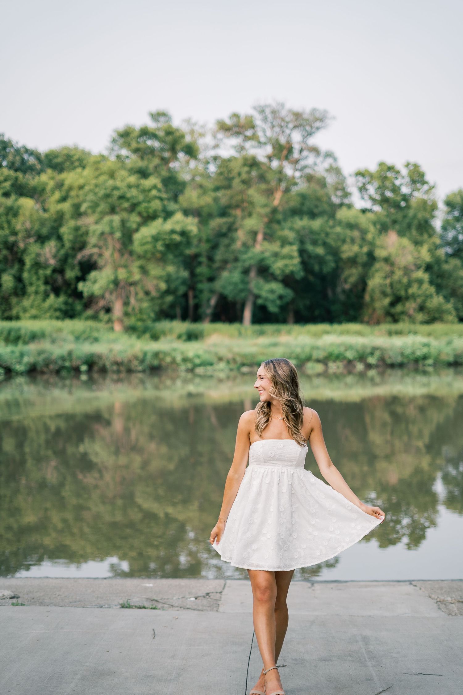 Flowing white dress movement sequence captured by a serene lake with trees in background.