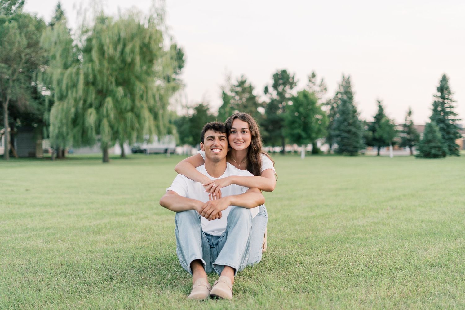 A couple embraces while sitting together in a lush green park on a sunny summer day.