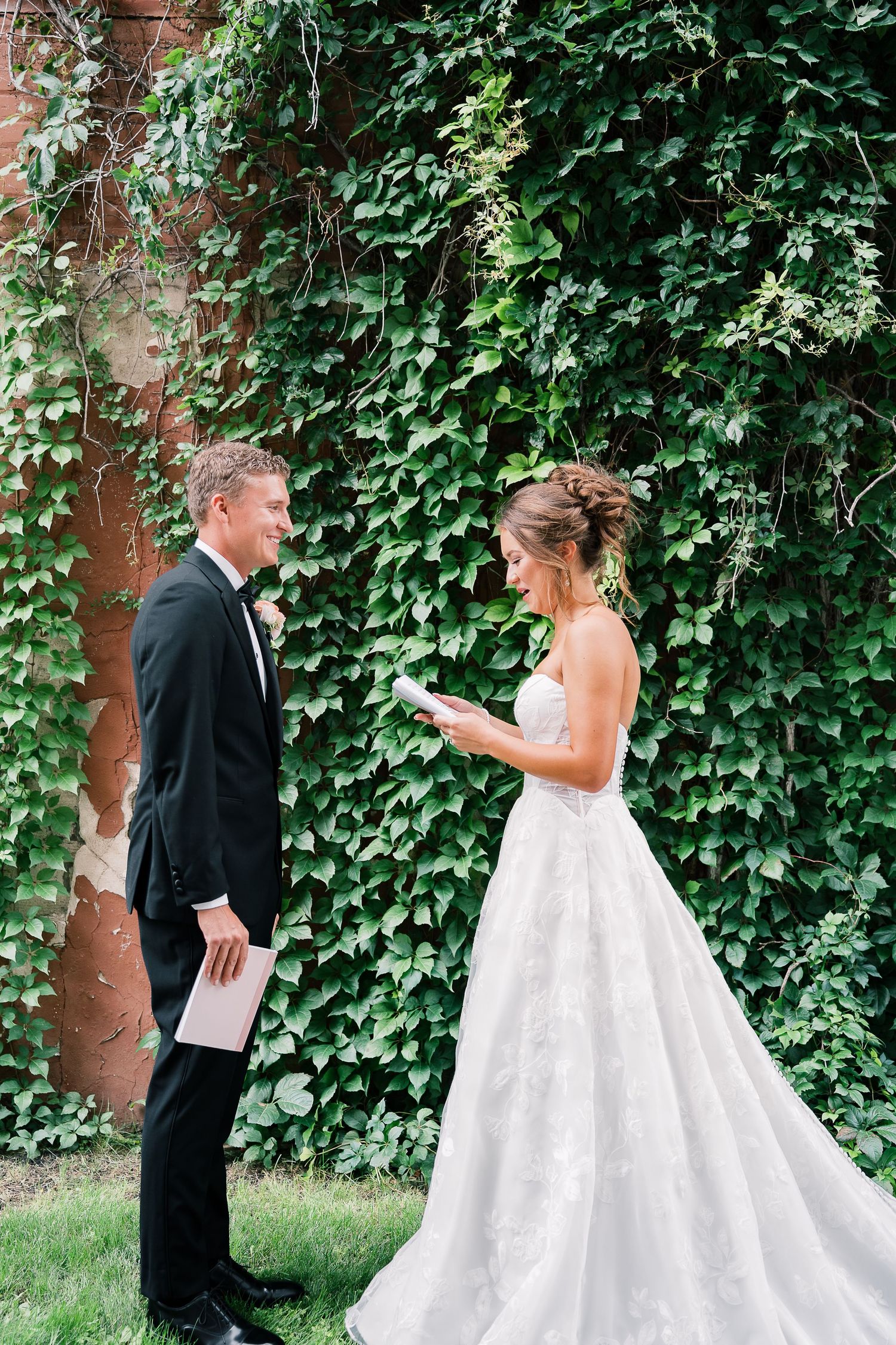 A couple shares a sweet first look moment in front of an ivy-covered wall during their wedding day.