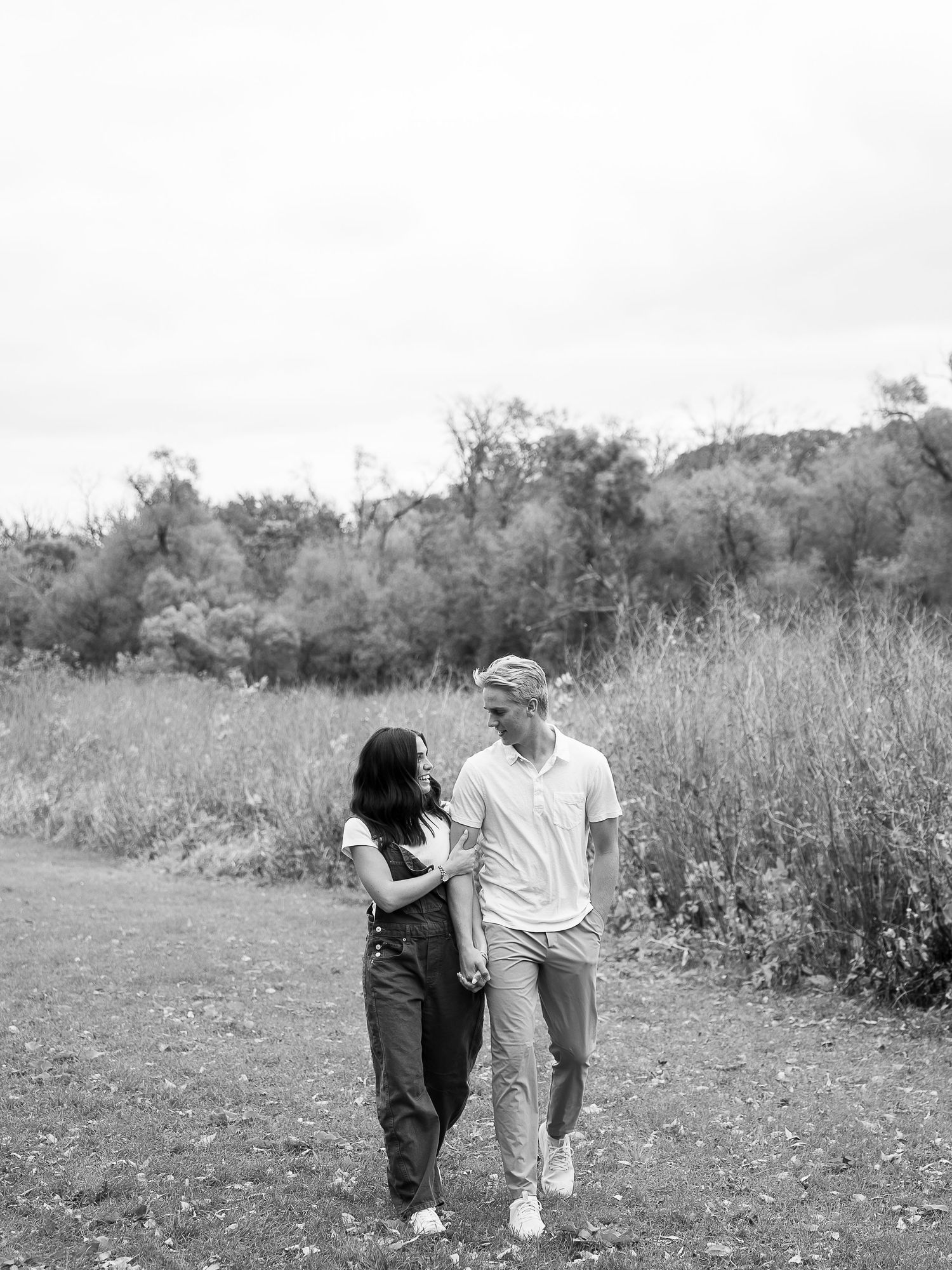 A couple shares a romantic moment while walking together in a wildflower meadow on a sunny day.