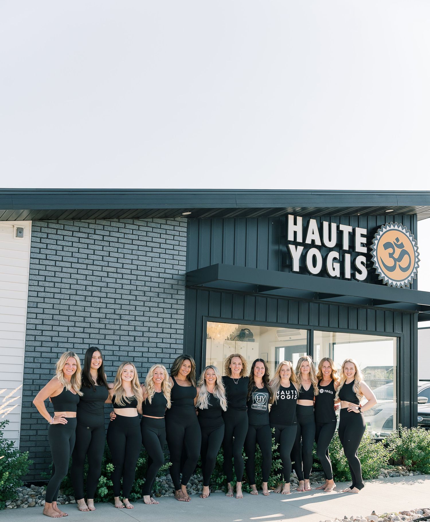 A large group of people wearing black outfits pose together outside a storefront with Yogis signage.