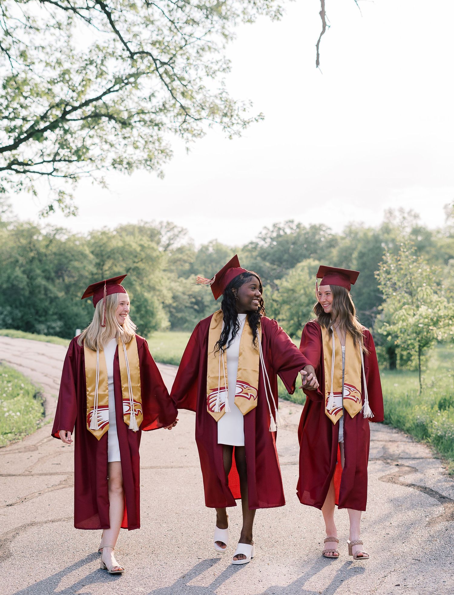 Three graduates walking together in burgundy caps and gowns.