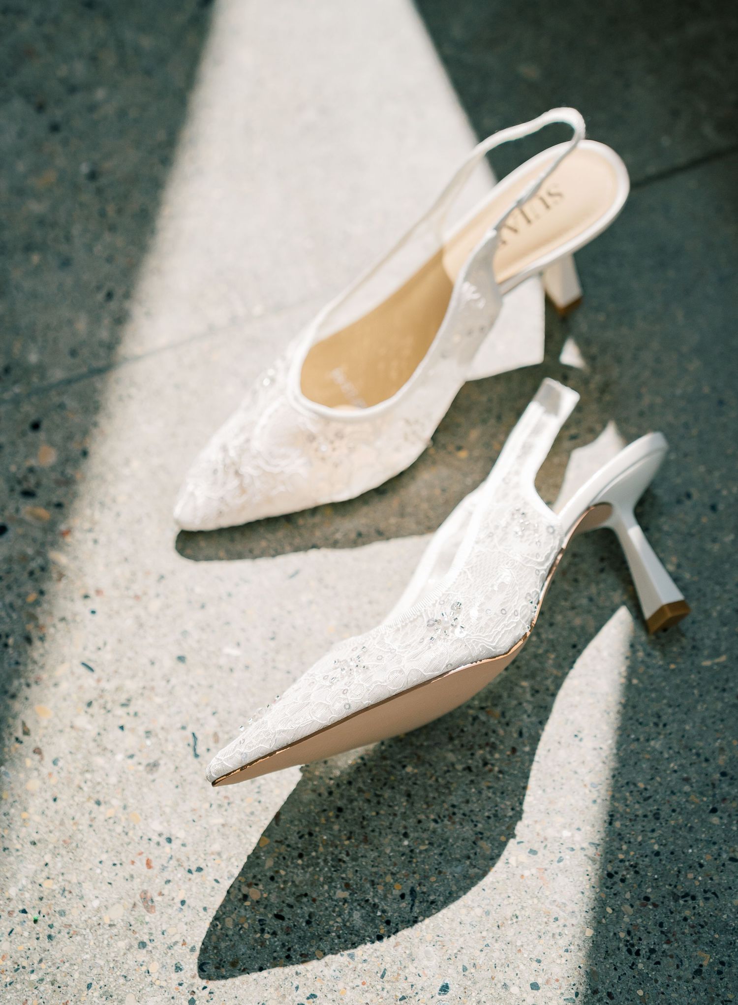 A elegant white lace slingback bridal heel displayed from multiple angles on a concrete surface.