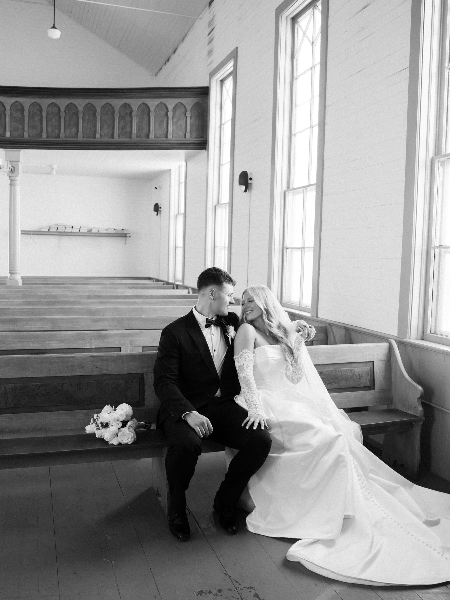 Black and white photo of bride and groom sharing an intimate moment seated in a church pew on their wedding day.