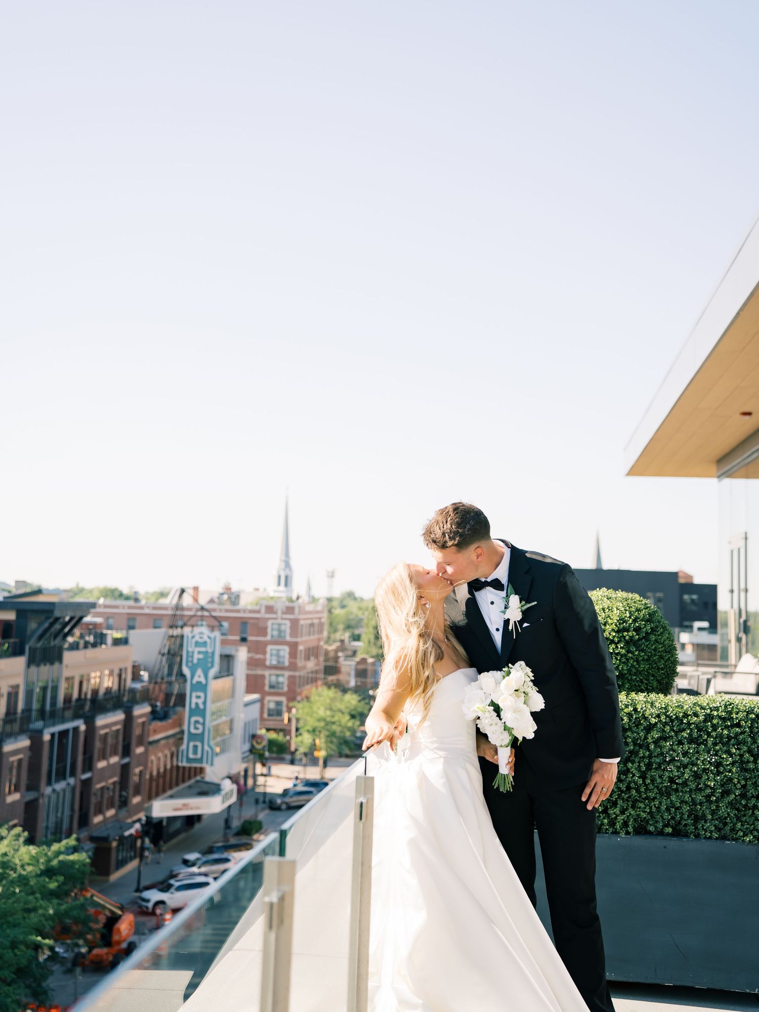Bride and groom share a romantic rooftop kiss with the Fargo Theatre sign and city skyline visible behind them.