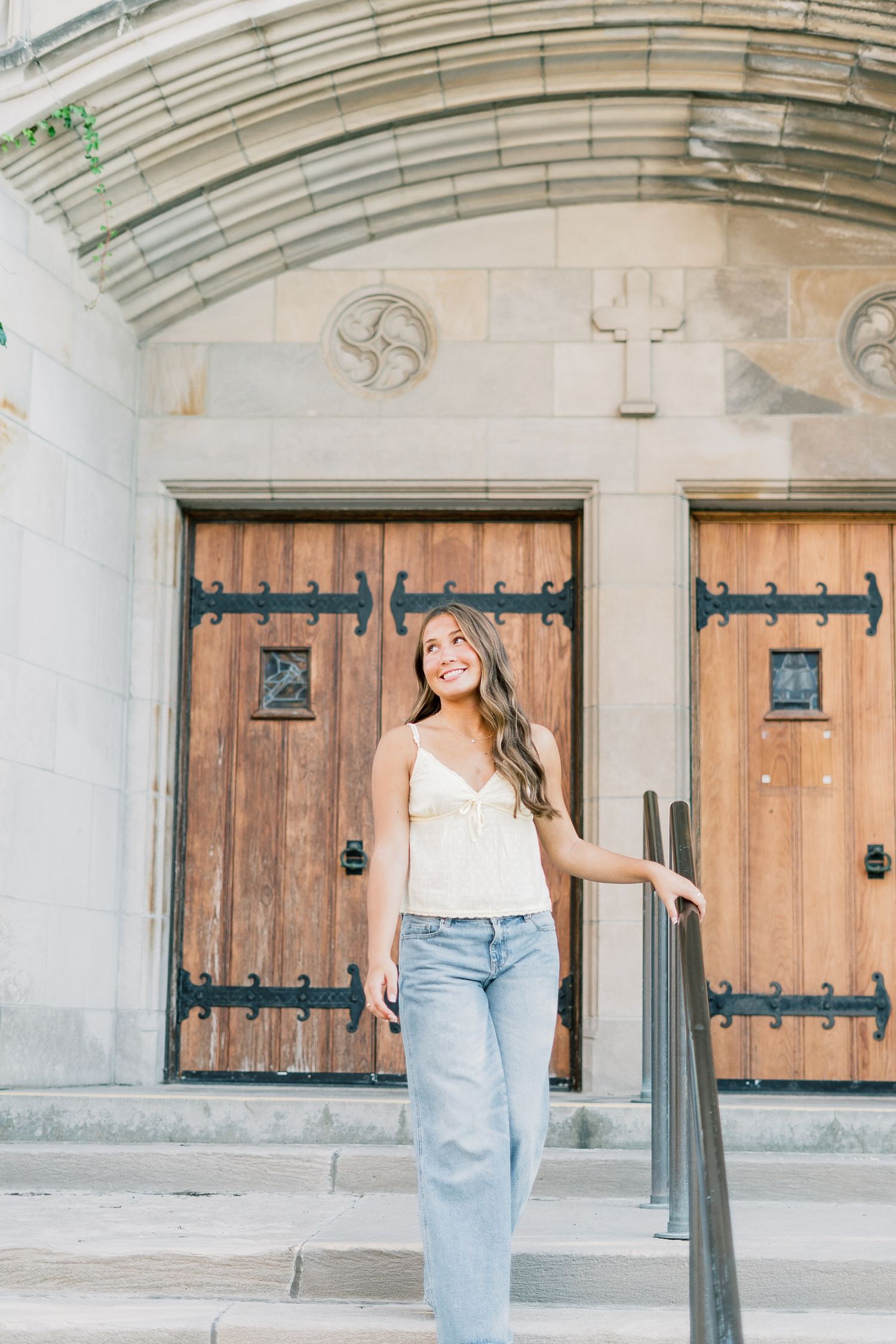 A person in light summer attire poses in front of rustic wooden church doors with decorative iron hinges.