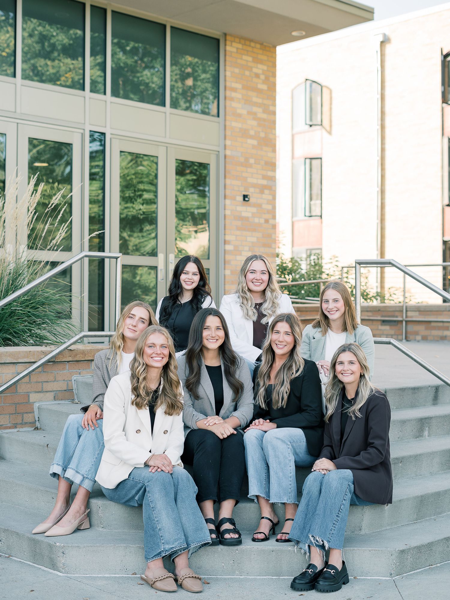 A group of friends sitting casually on outdoor concrete steps wearing jeans and casual attire in similar poses.