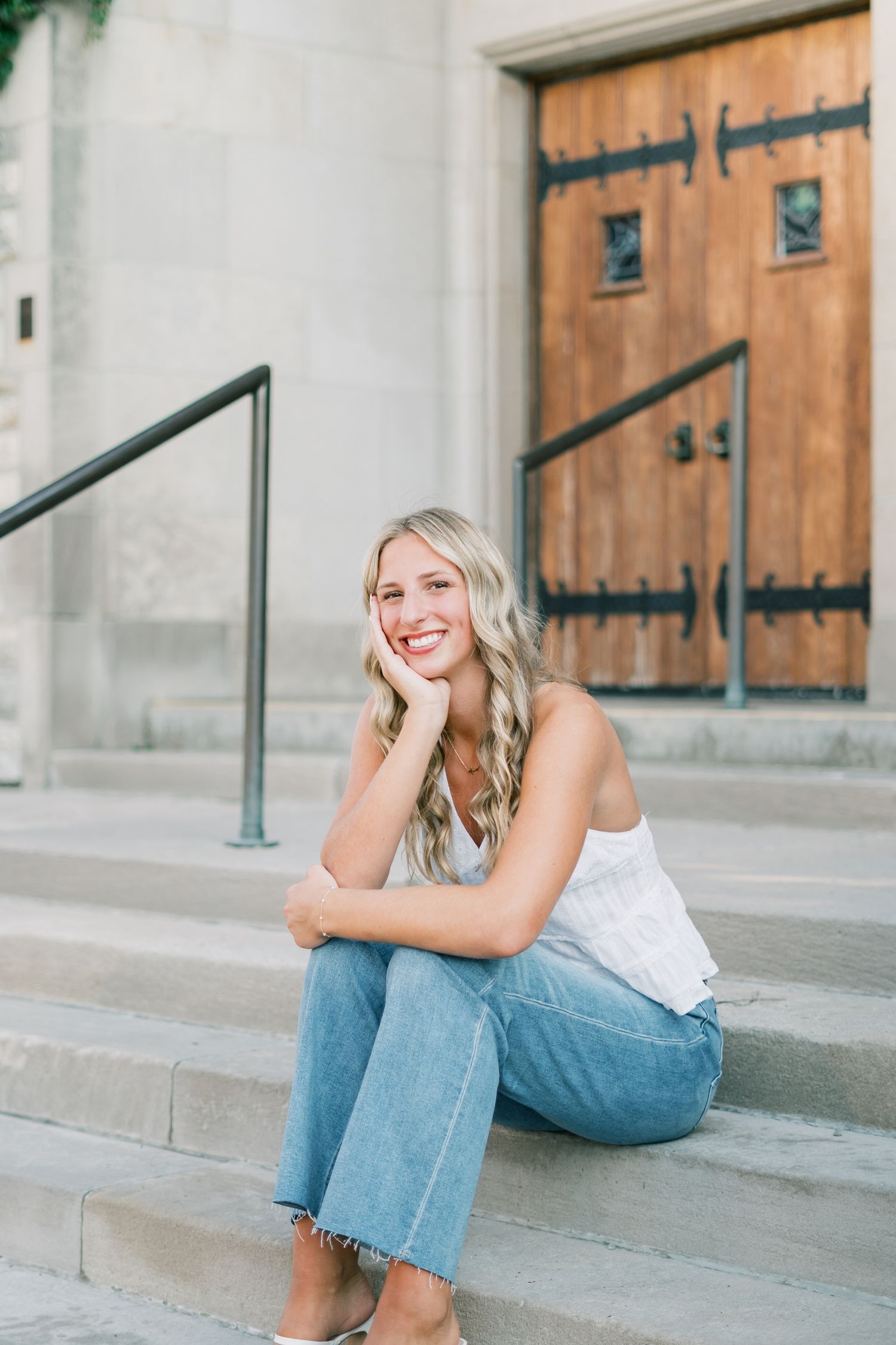 Person in casual attire sitting on concrete steps with rustic wooden doors in the background.