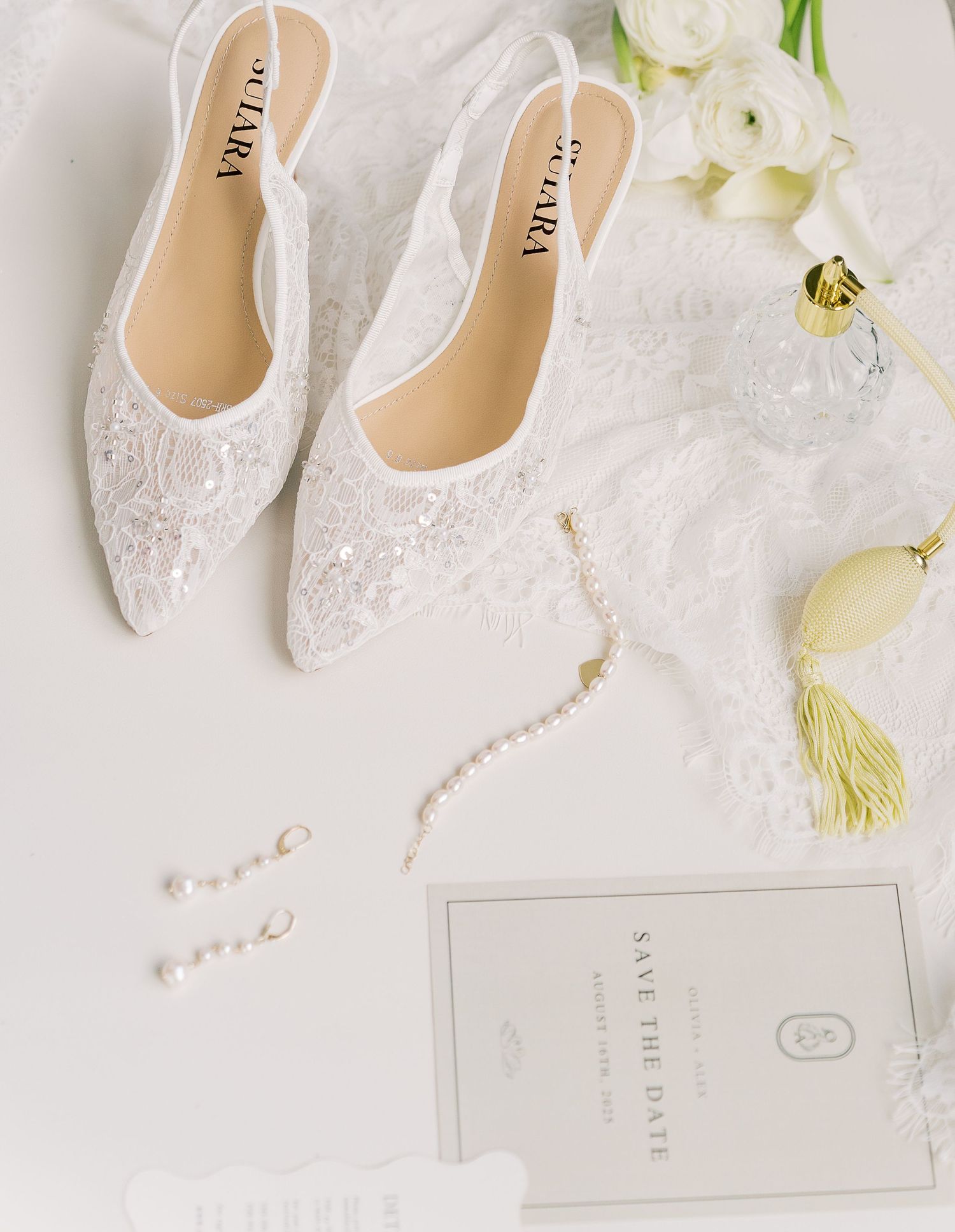Elegant white bridal flats adorned with delicate lace and pearls arranged against a light backdrop with white roses.