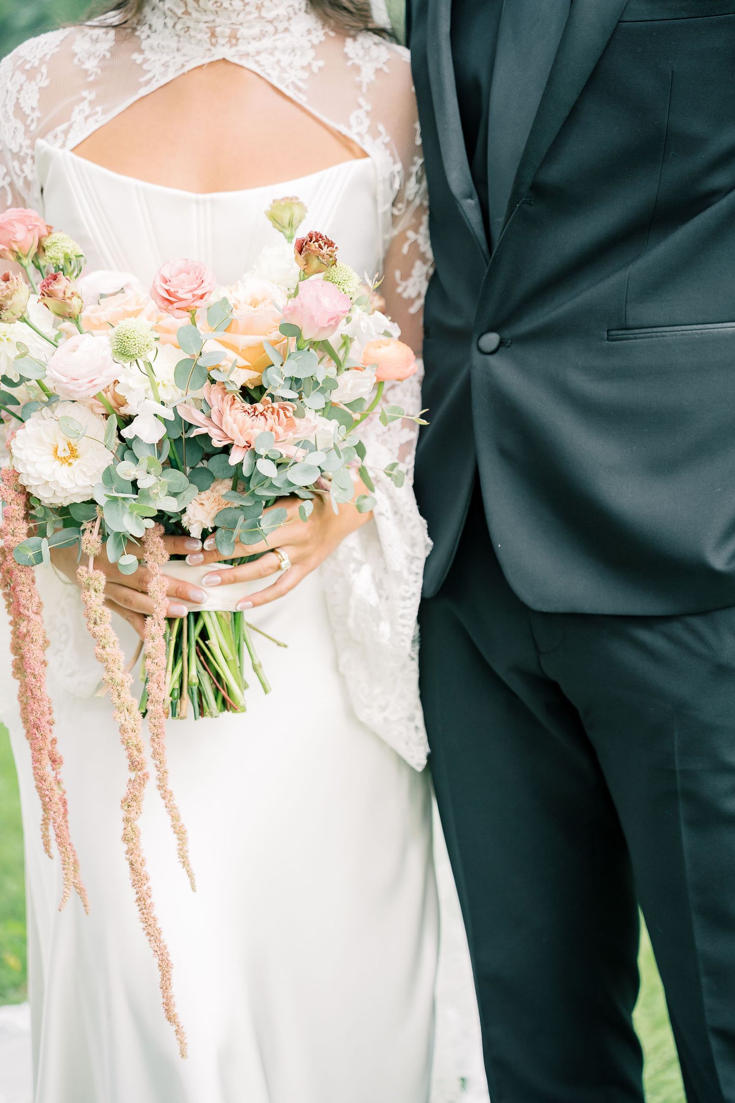 Wedding party members in black suits and white dresses hold delicate peach and ivory floral bouquets.