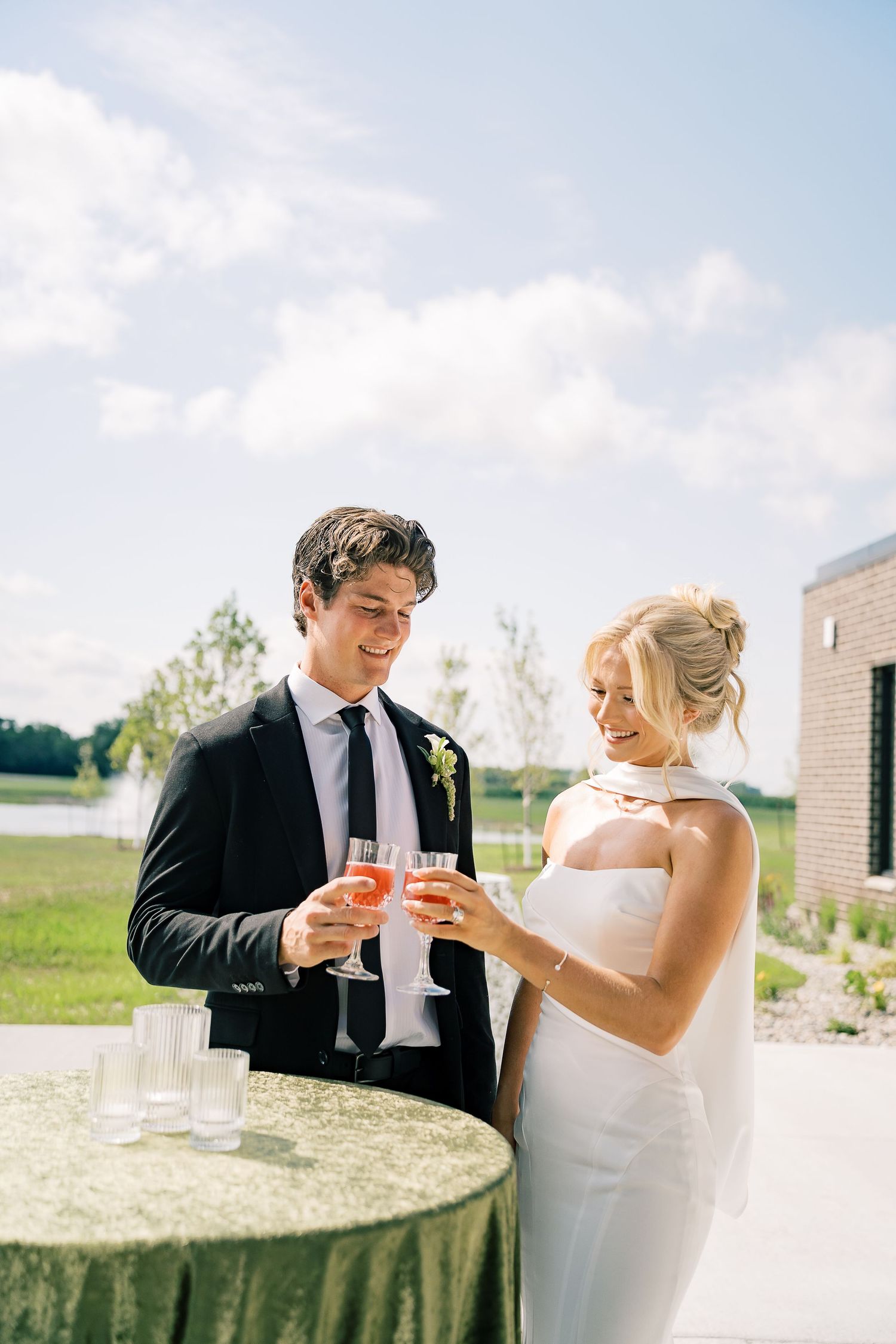 A couple shares an intimate toast with champagne glasses on their wedding day in the countryside.