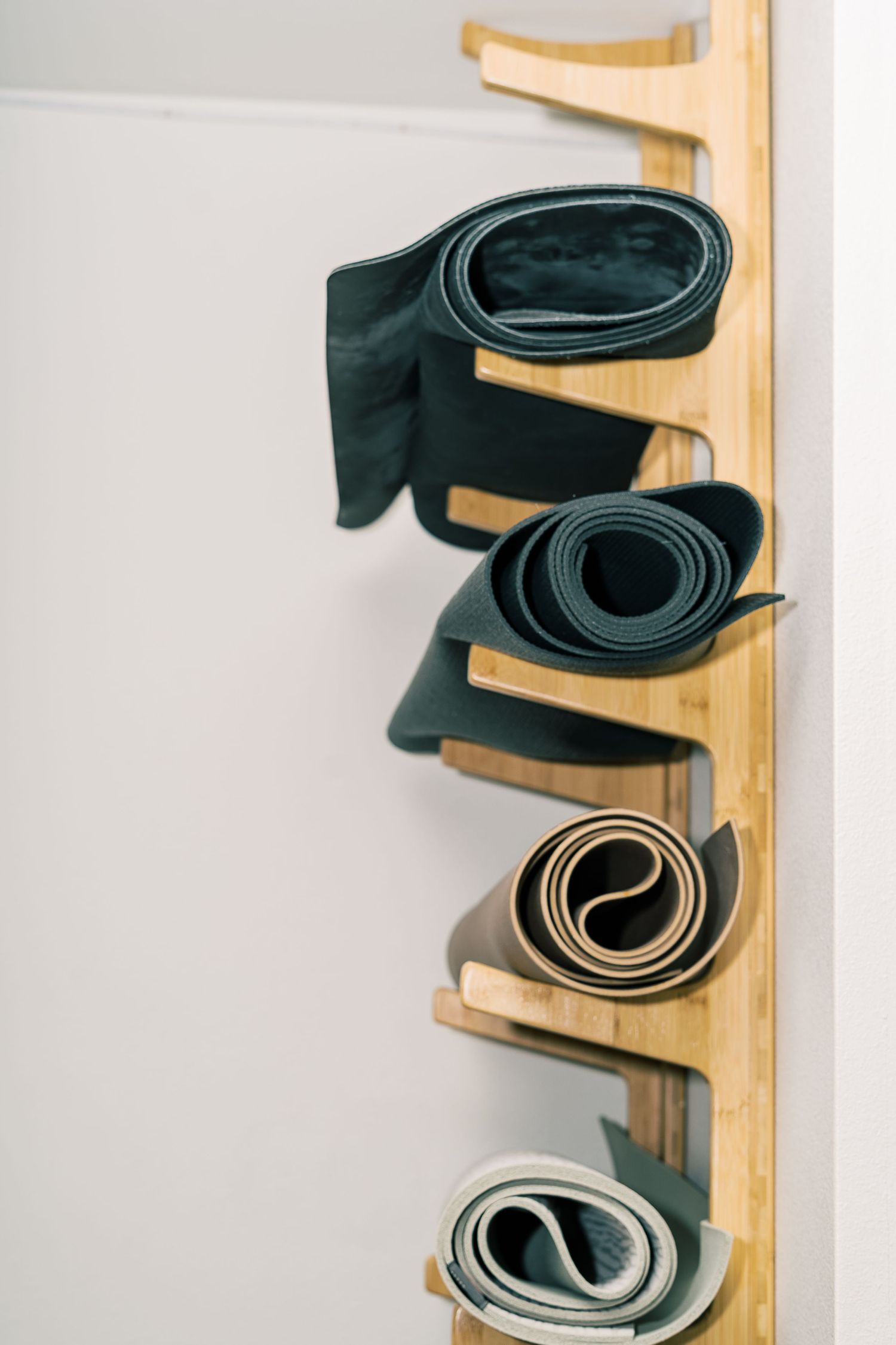 Rolled up yoga mats organized vertically on a wooden wall-mounted storage rack.