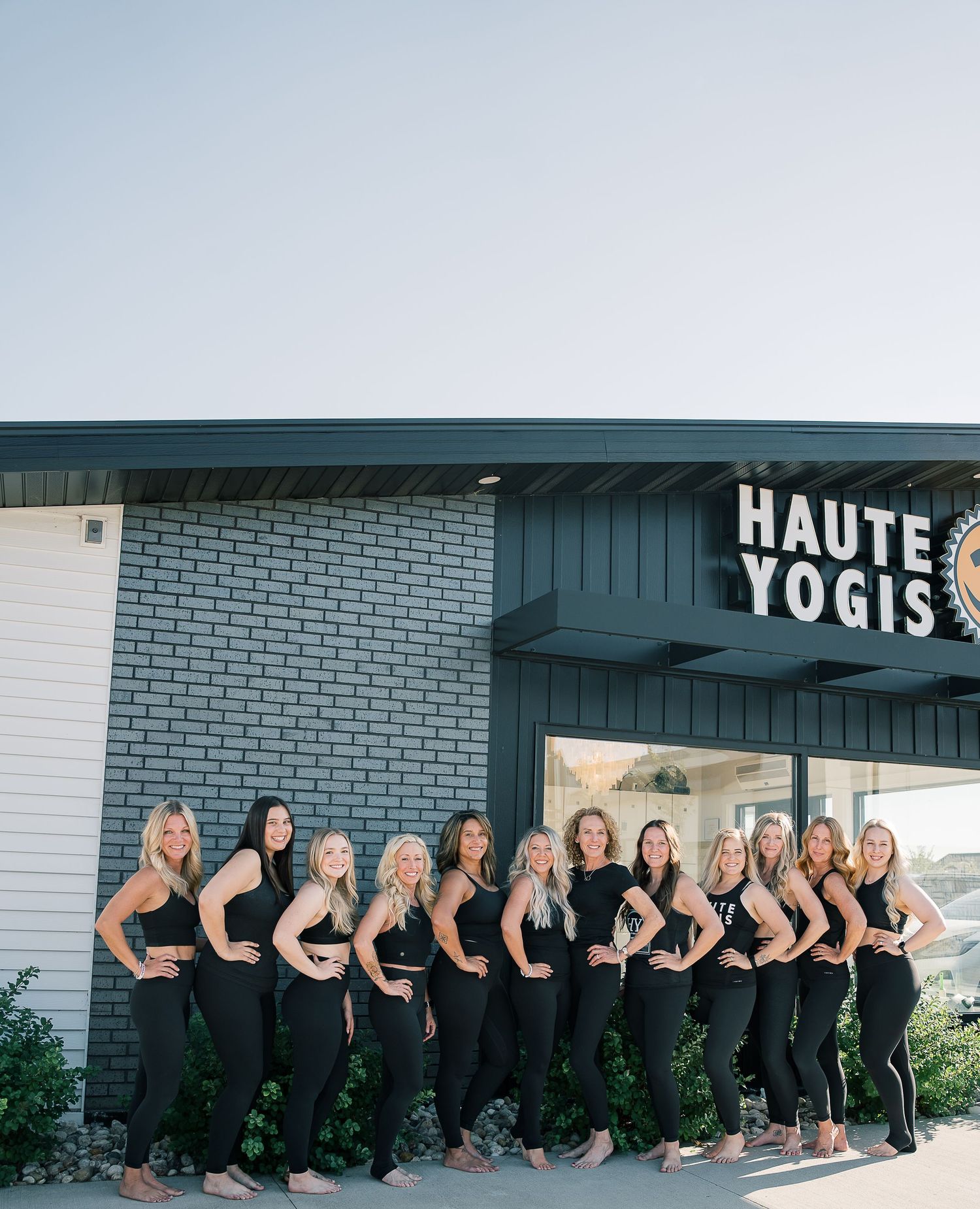A group of fitness instructors in matching black athletic wear pose together outside Haute Yogis studio.